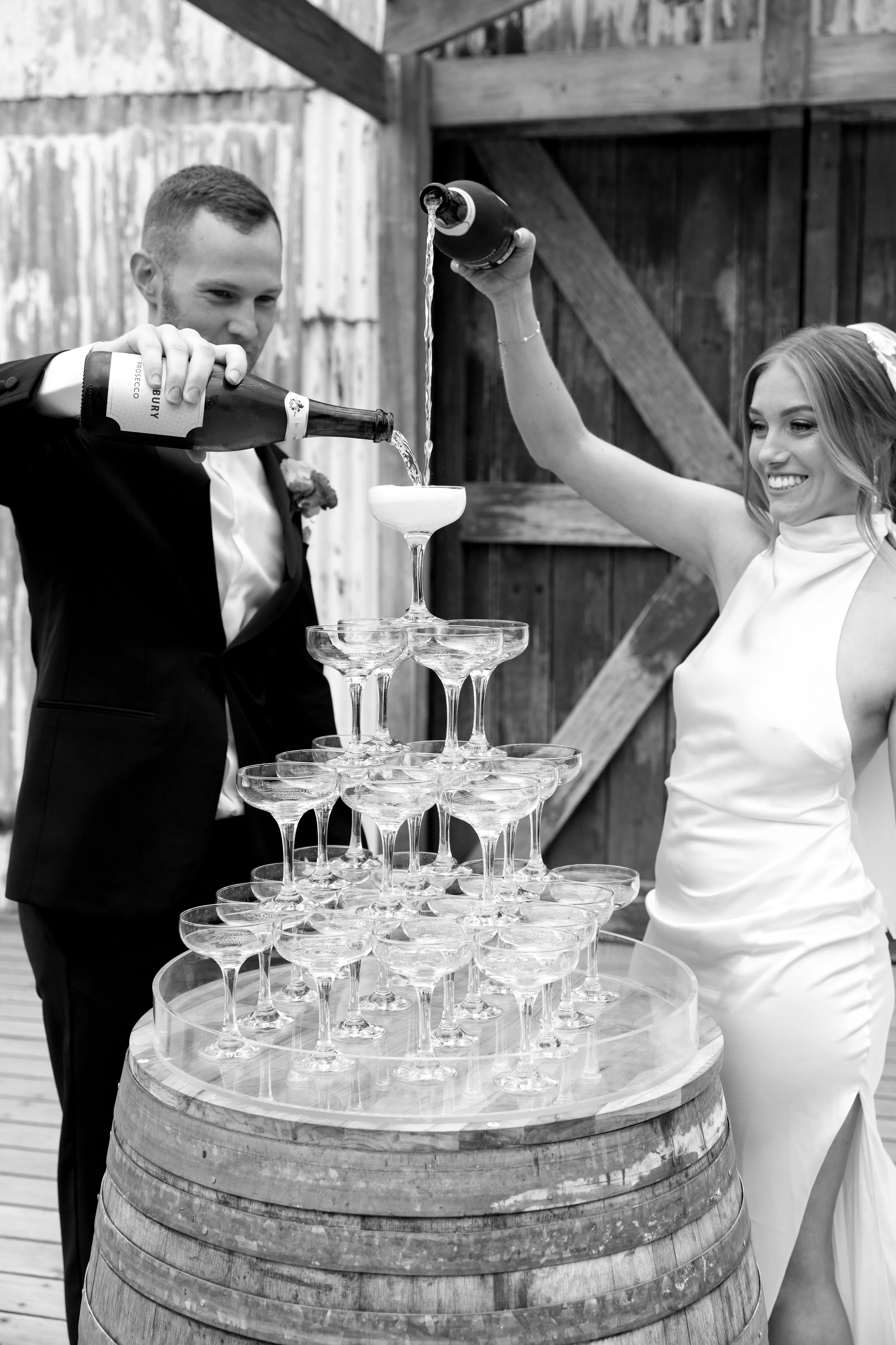 Bride in a silk wedding gown and groom pouring champagne into a glass pyramid, celebrating after expert bridal alterations in Melbourne