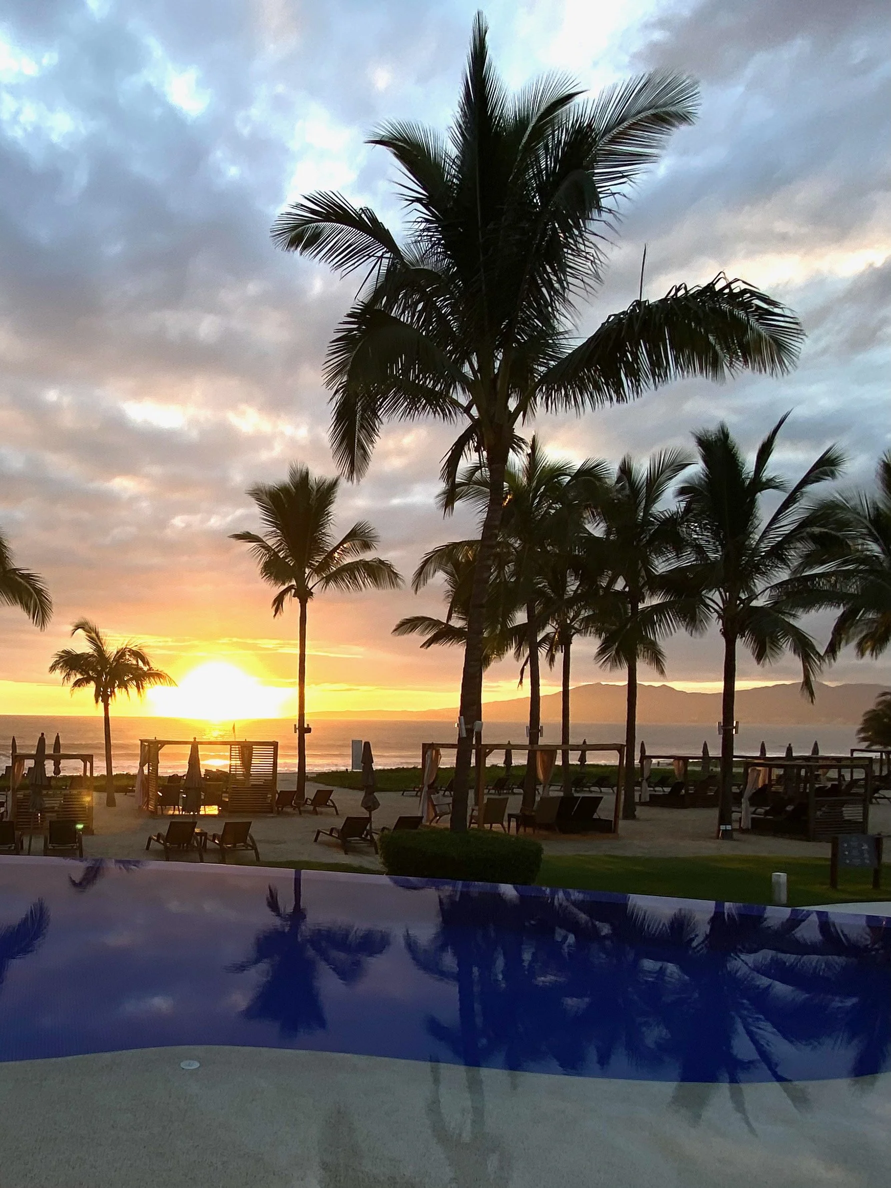 Sunset over a resort pool with palm trees and ocean views — Miller Travel Group curated all-inclusive experiences