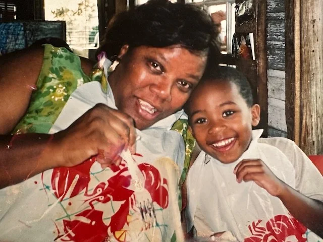 A woman and a young boy sitting at a table, smiling and enjoying a meal together in a rustic setting.