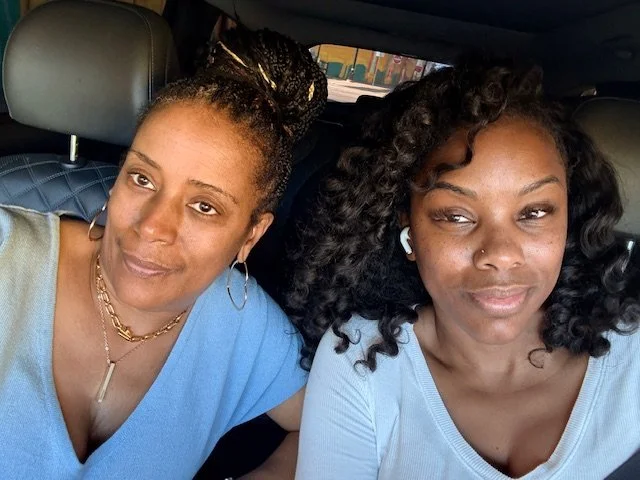 Two women taking a selfie inside a vehicle, sitting in the front seats.