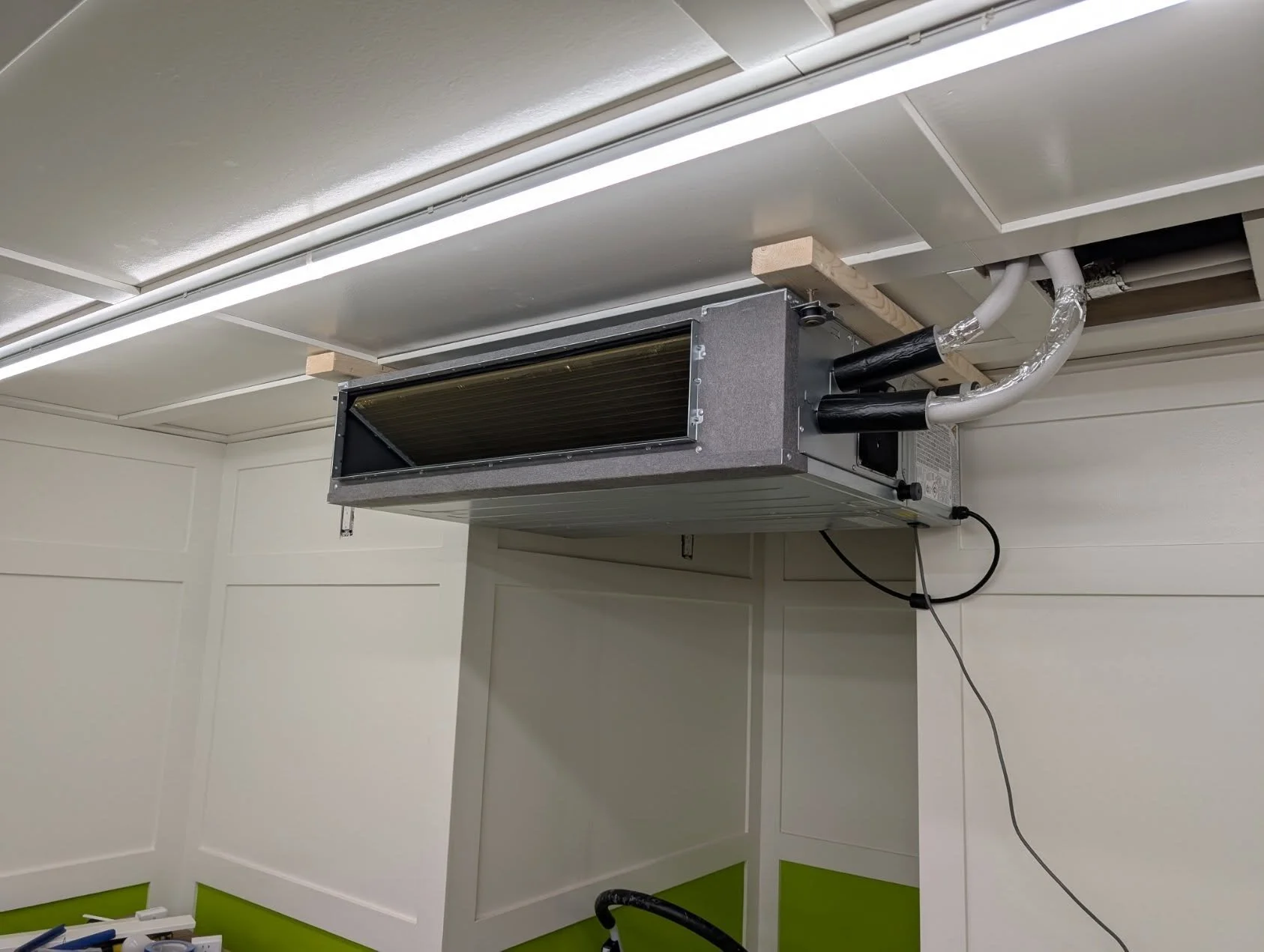 Indoor HVAC ductless mini-split air conditioning unit outside the ceiling in a room, with electrical wires and pipes connected.