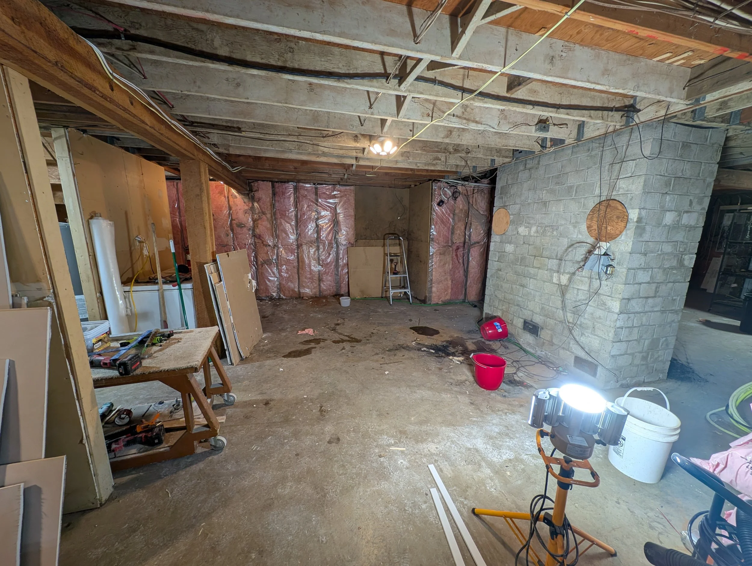 Underground basement with exposed ceiling beams, construction tools, insulation, and partially finished walls.