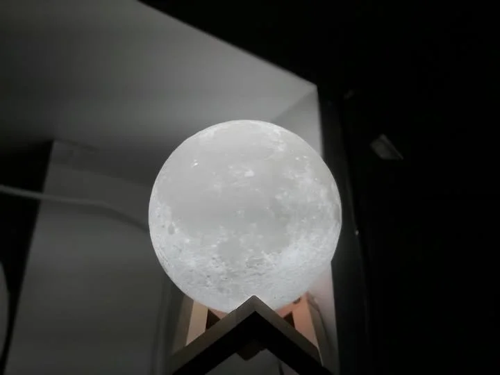 Illuminated moon-shaped lamp on a wooden stand, set against a dark wall in a room.