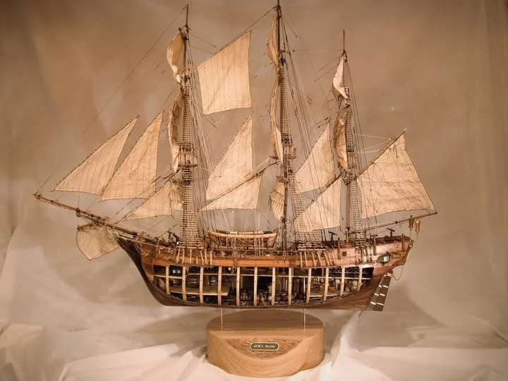 Model of a large sailing ship with multiple masts and sails, displayed on a wooden stand.