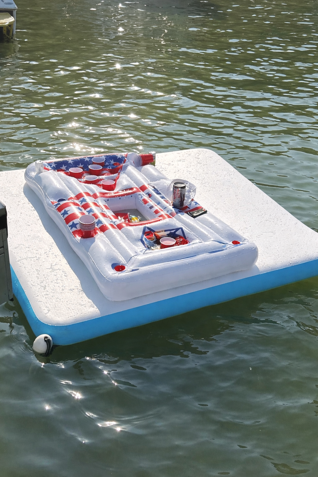 Inflatable float with an American flag design, surrounded by cups, on a dock over water.