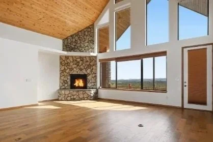 Spacious living room with large windows, a stone fireplace, and a wooden ceiling.