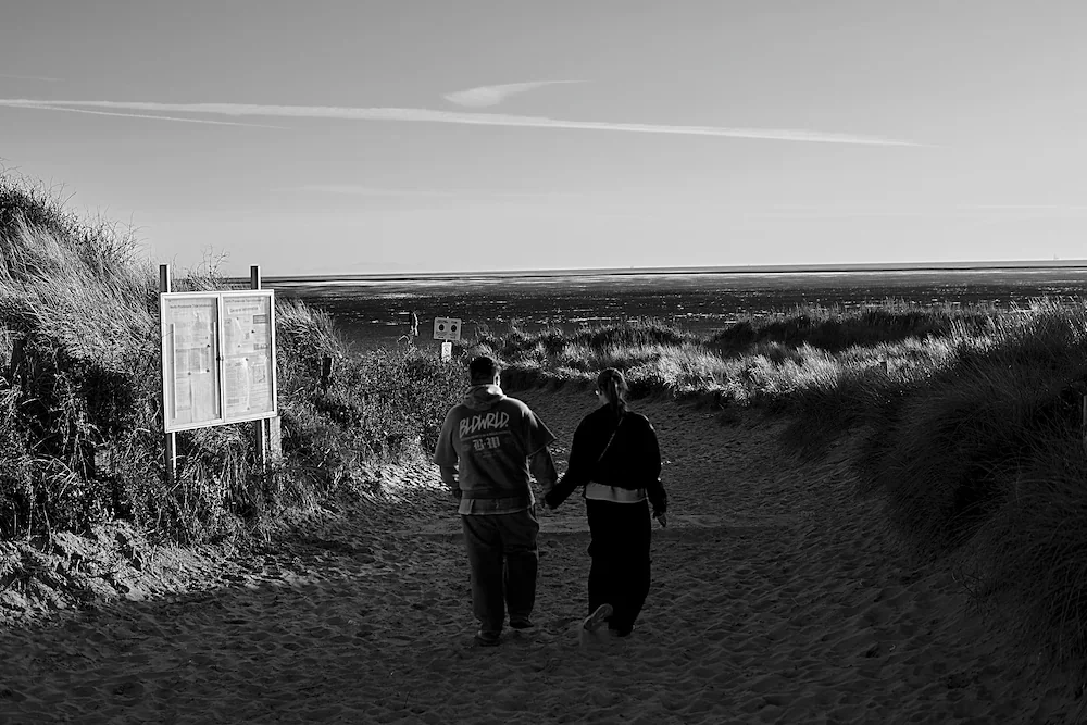 northwest-coast-couple-walking-sand-dunes-lancashire-bw.webp