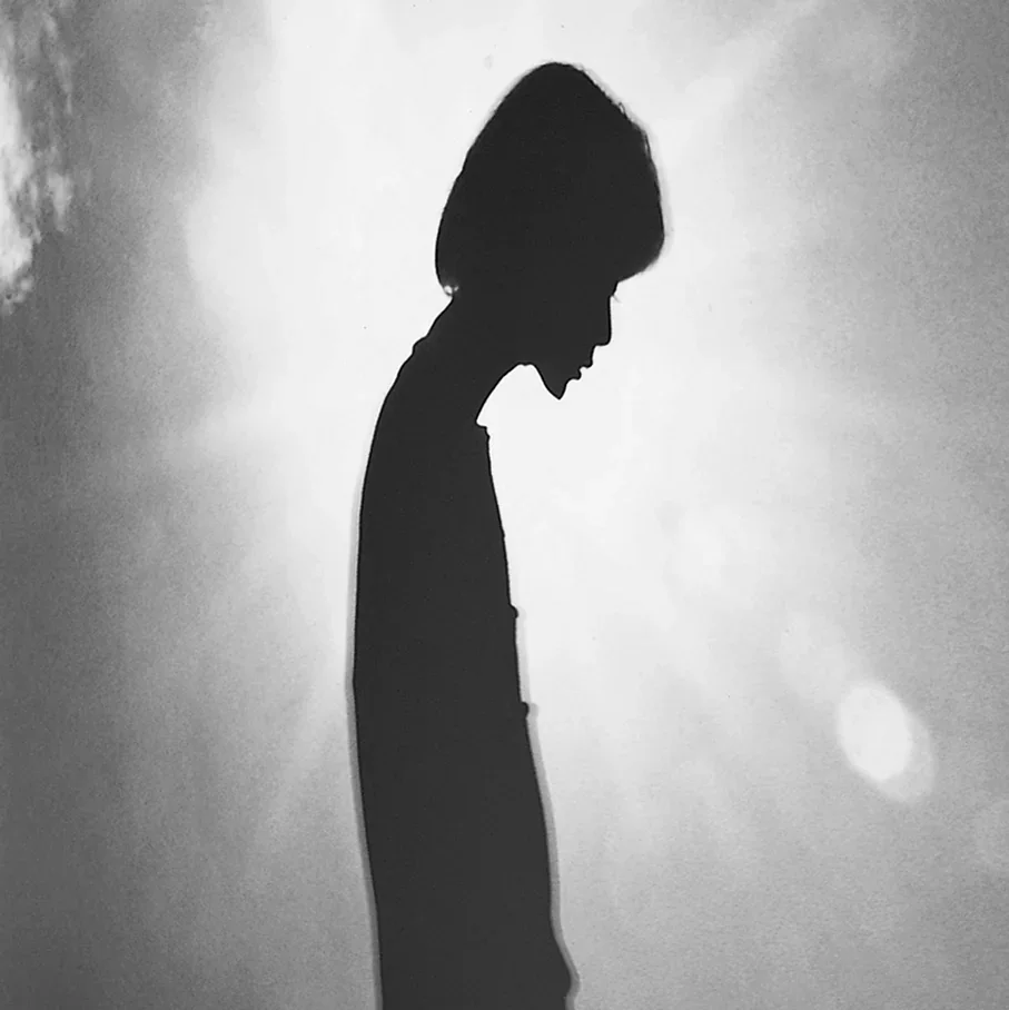 A black and white silhouette of a woman with her head bowed, standing against a plain background.