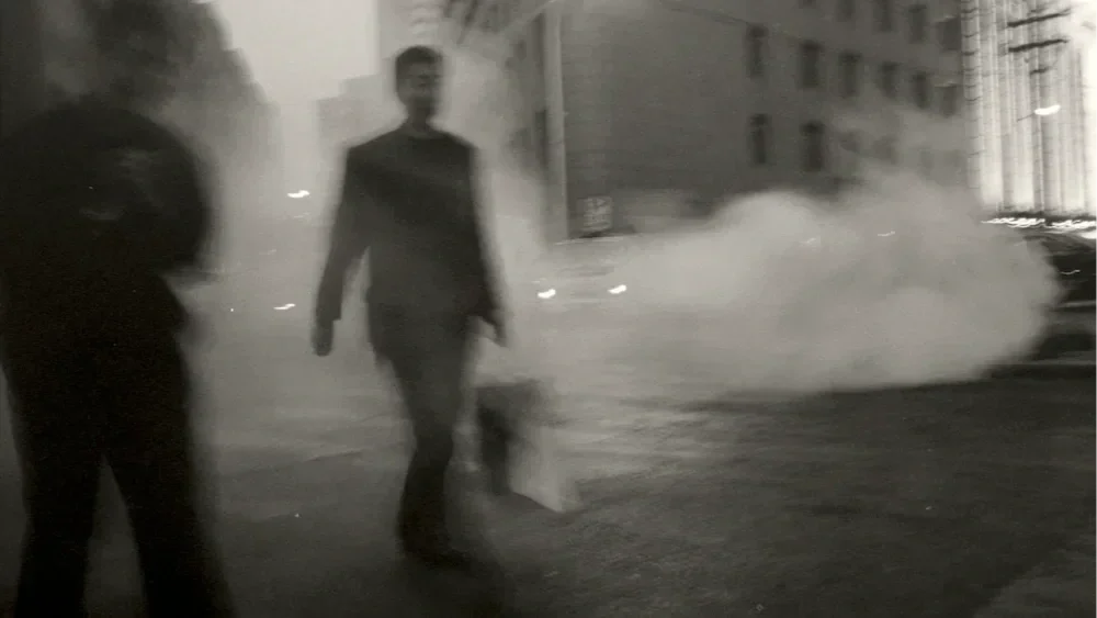 Two people walking on a city street at night, with steam rising from the sidewalk.