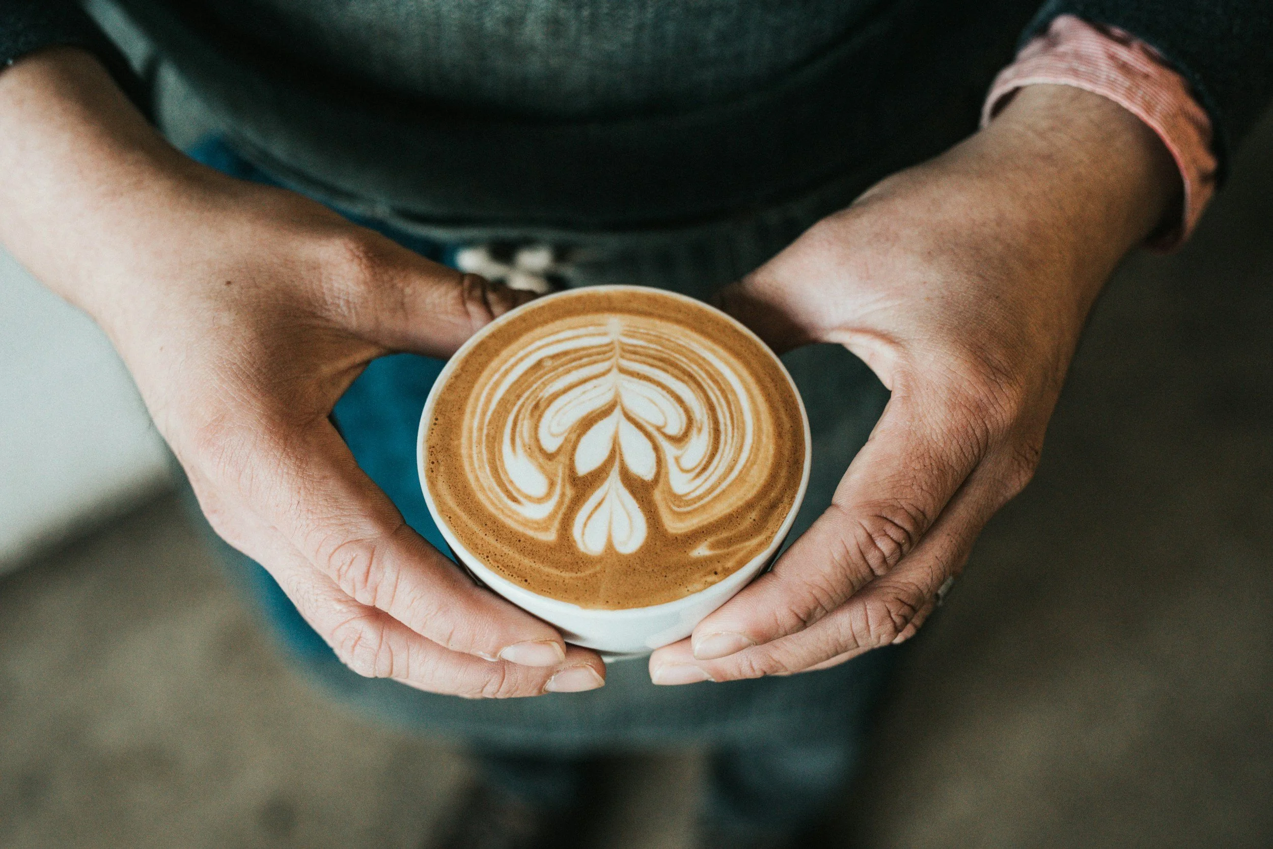 Hands holding a cup of coffee with latte art resembling a floral pattern.
