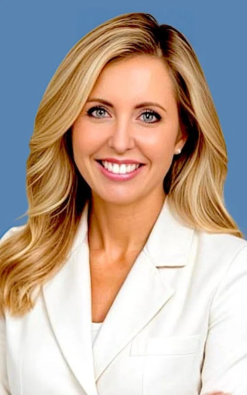 A smiling blonde woman with blue eyes, wearing a white blazer, against a blue background.