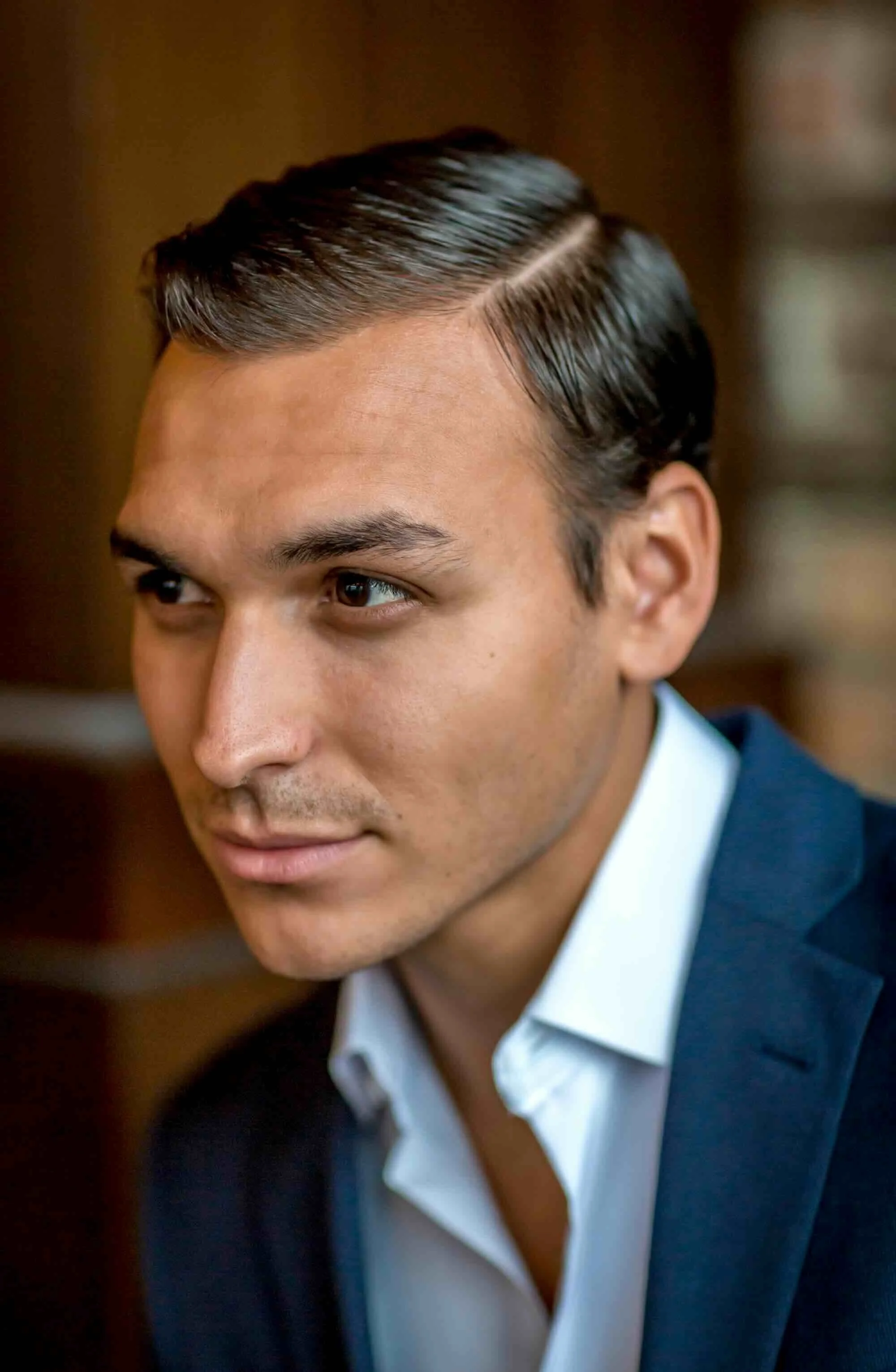 Close-up of a man with slicked-back hair wearing a suit and white shirt, looking to the side.