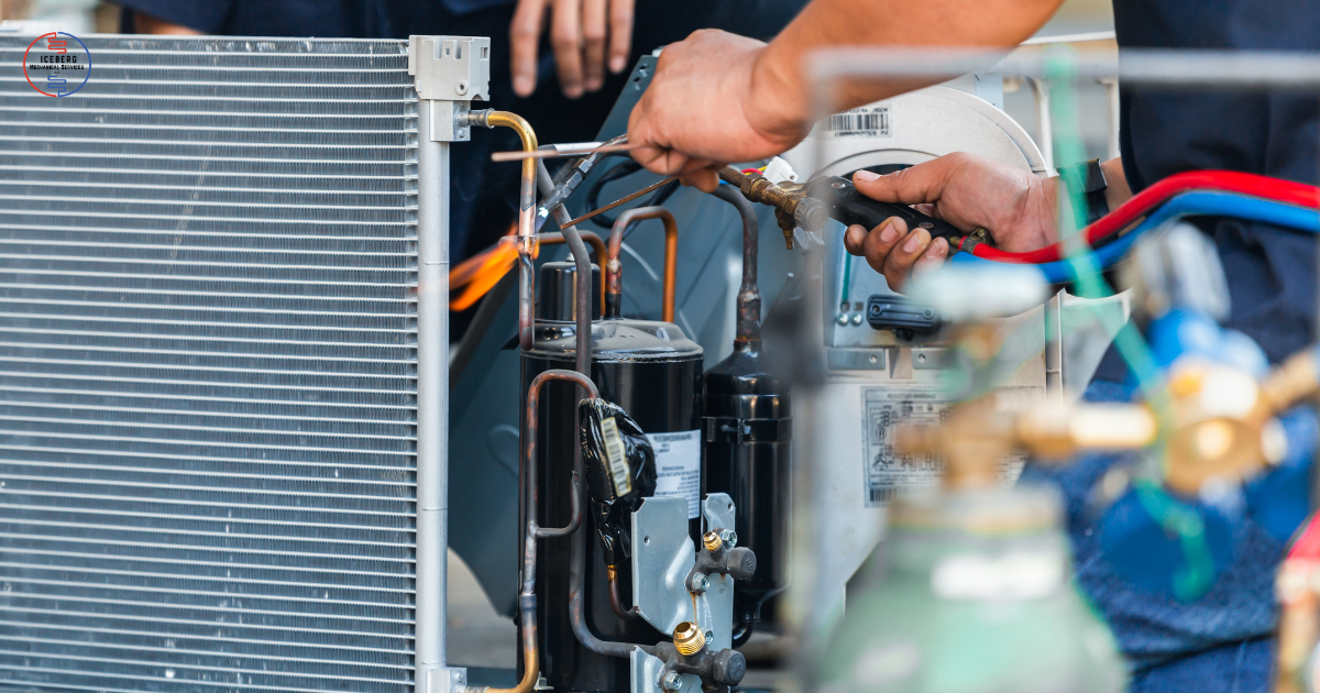 Technician repairing an air conditioning unit while holding a gauge manifold, with the unit's condenser coil visible on the left.