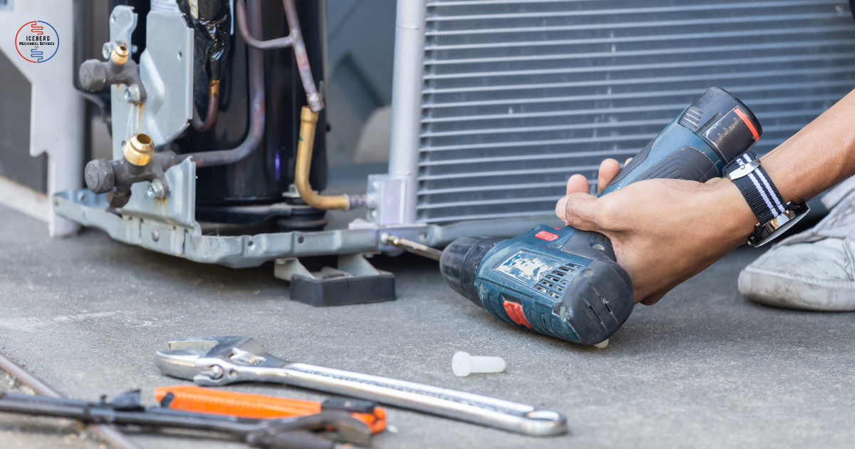 A person using a cordless drill on an air conditioning unit outside, with tools like a wrench and screwdriver nearby.