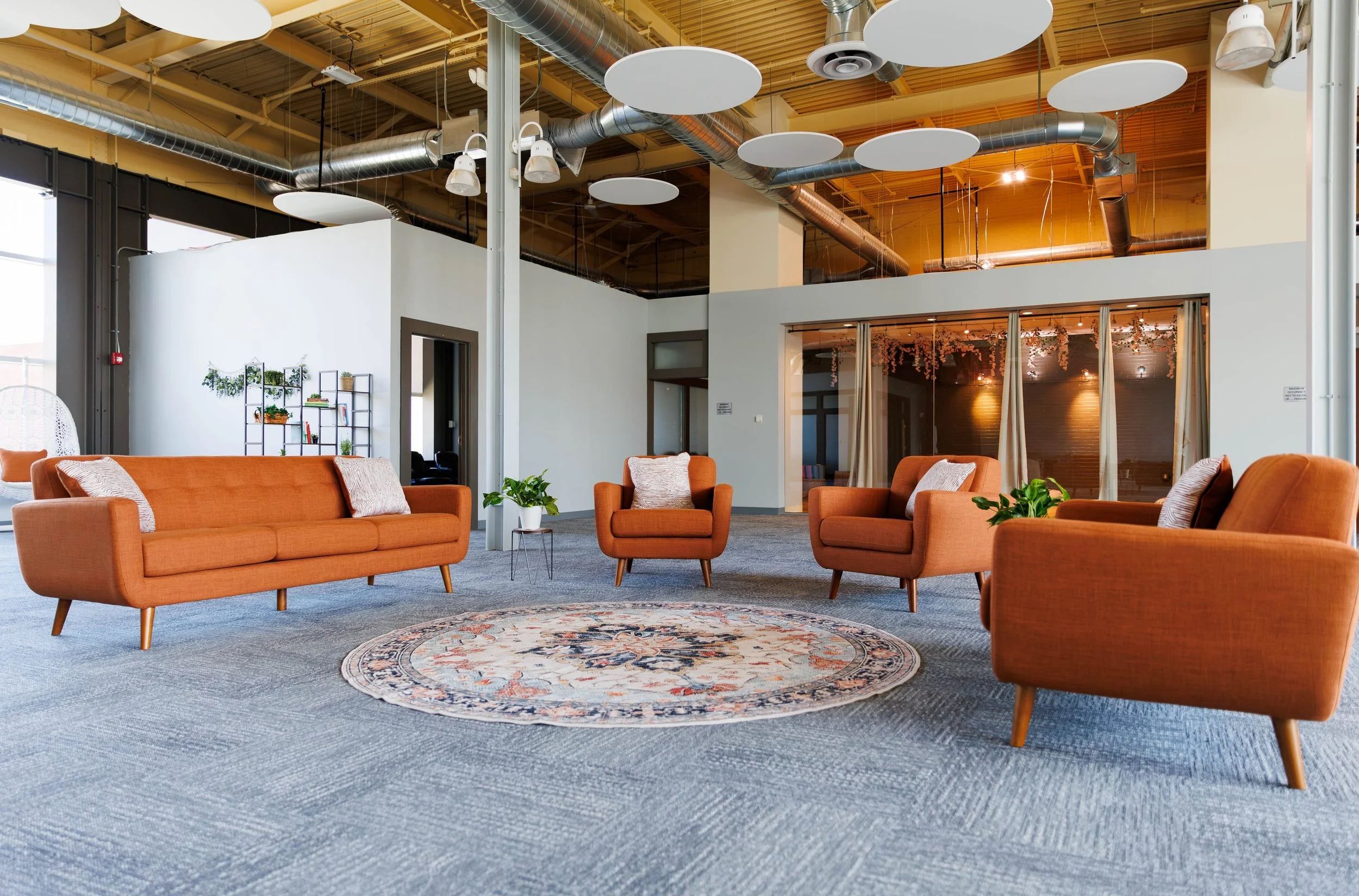 Aurora’s modern lounge area with orange chairs, a round rug, plants, and high ceilings in our calm outpatient treatment setting.