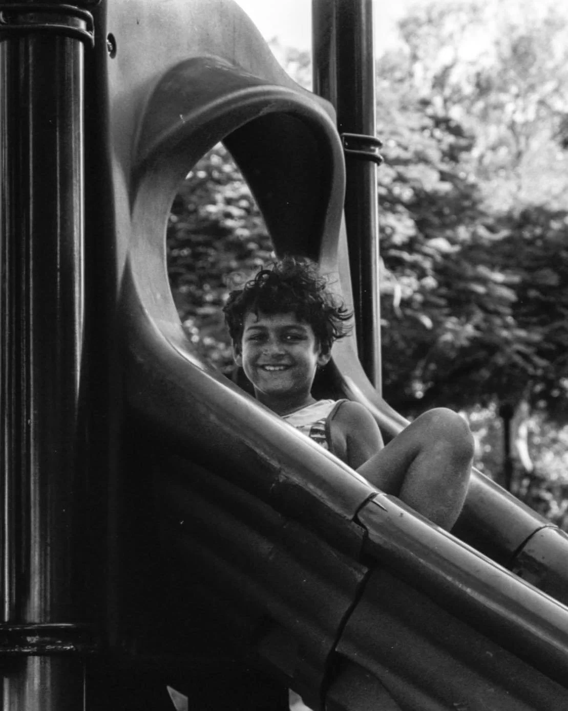 Child with curly hair smiling while sliding down a playground slide.