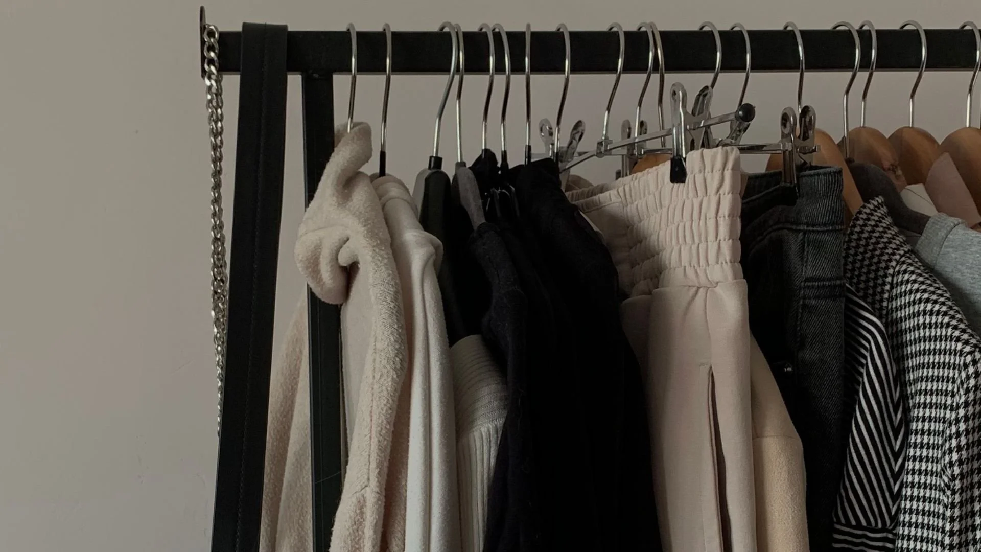 Clothing rack with various garments including sweaters, pants, and shirts hanging on metal hangers.