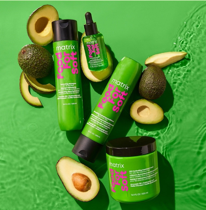 Three green bottles of Matrix food for soft hair care products, with avocado halves and whole avocados on a green background.