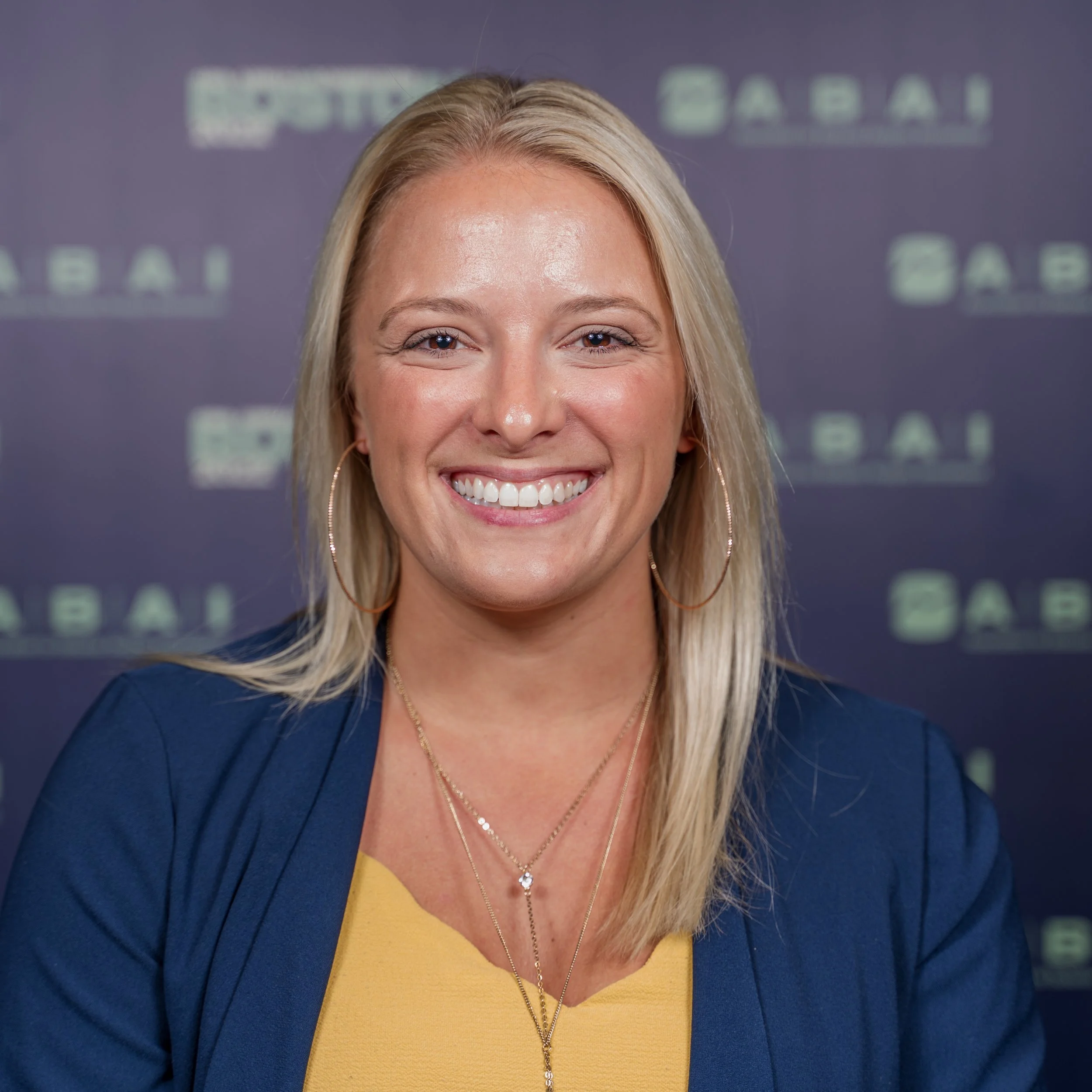 A woman with blonde hair smiling in front of a backdrop with the ABC logo.