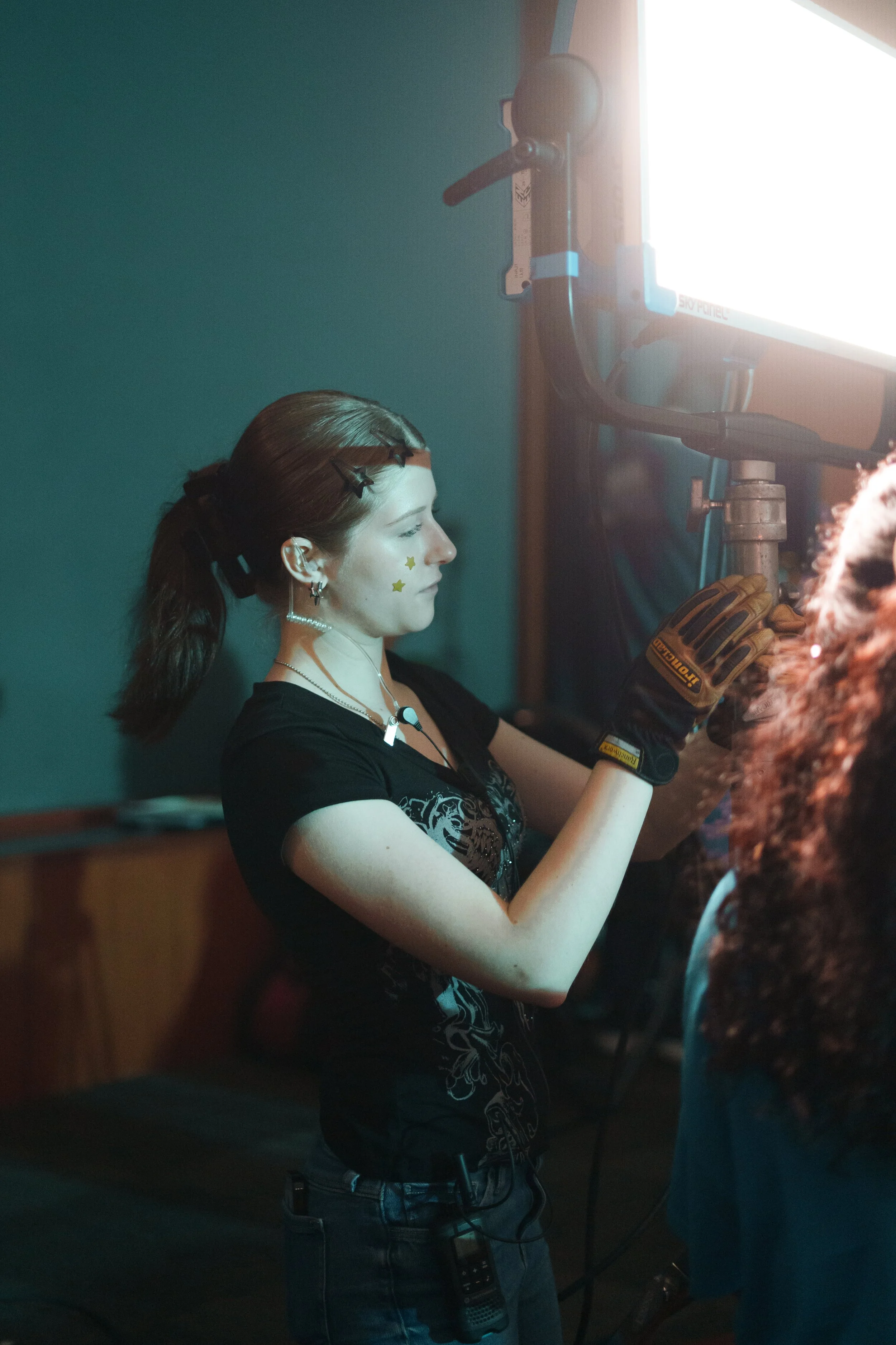 A woman operating a film or video camera, wearing gloves and earphones, with special star stickers on her face.