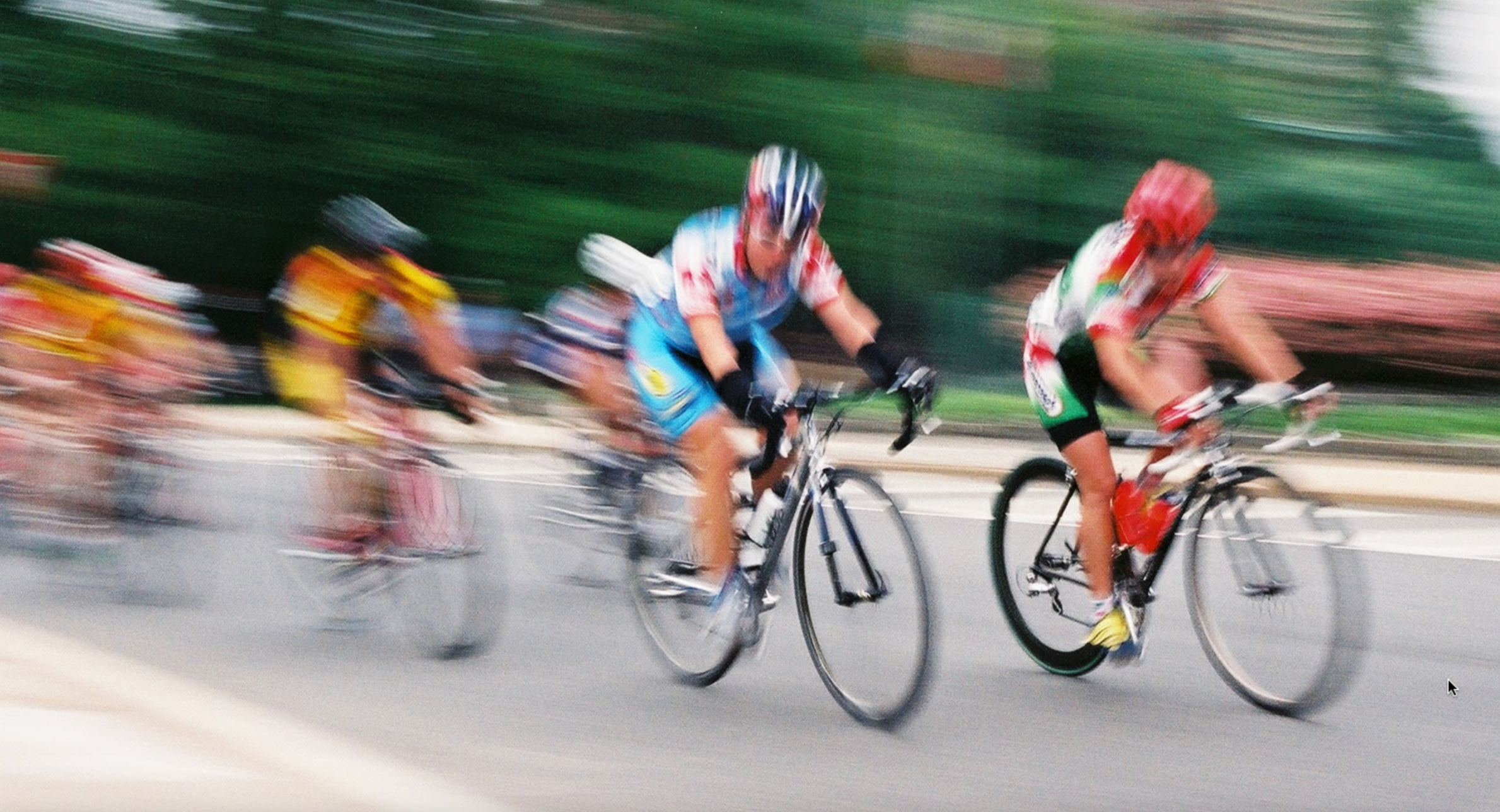 A group of professional cyclists racing on a road, with motion blur highlighting their speed.