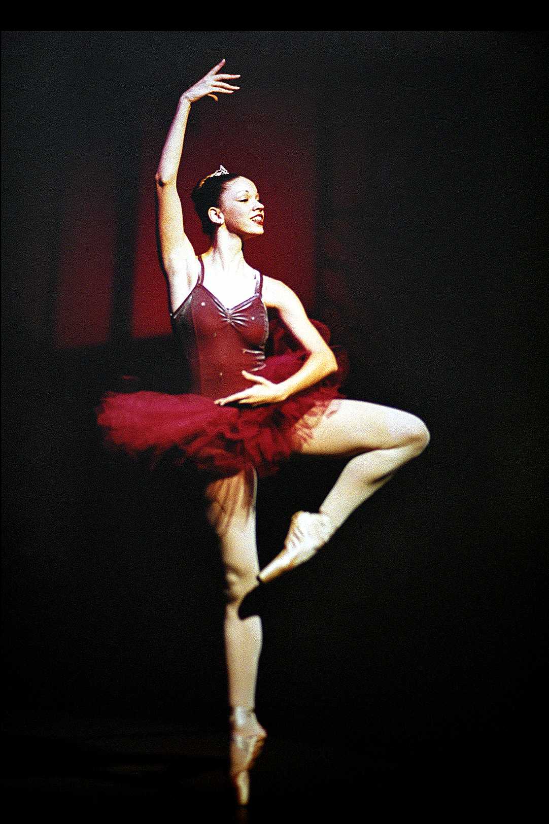 A ballerina in a red tutu performing a ballet pose on stage.