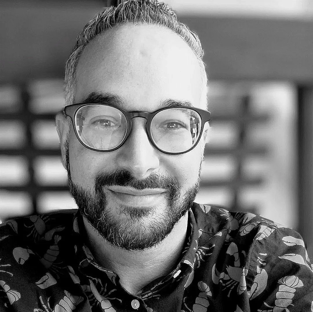 A man with glasses and a beard smiling at the camera in a black and white photo.
