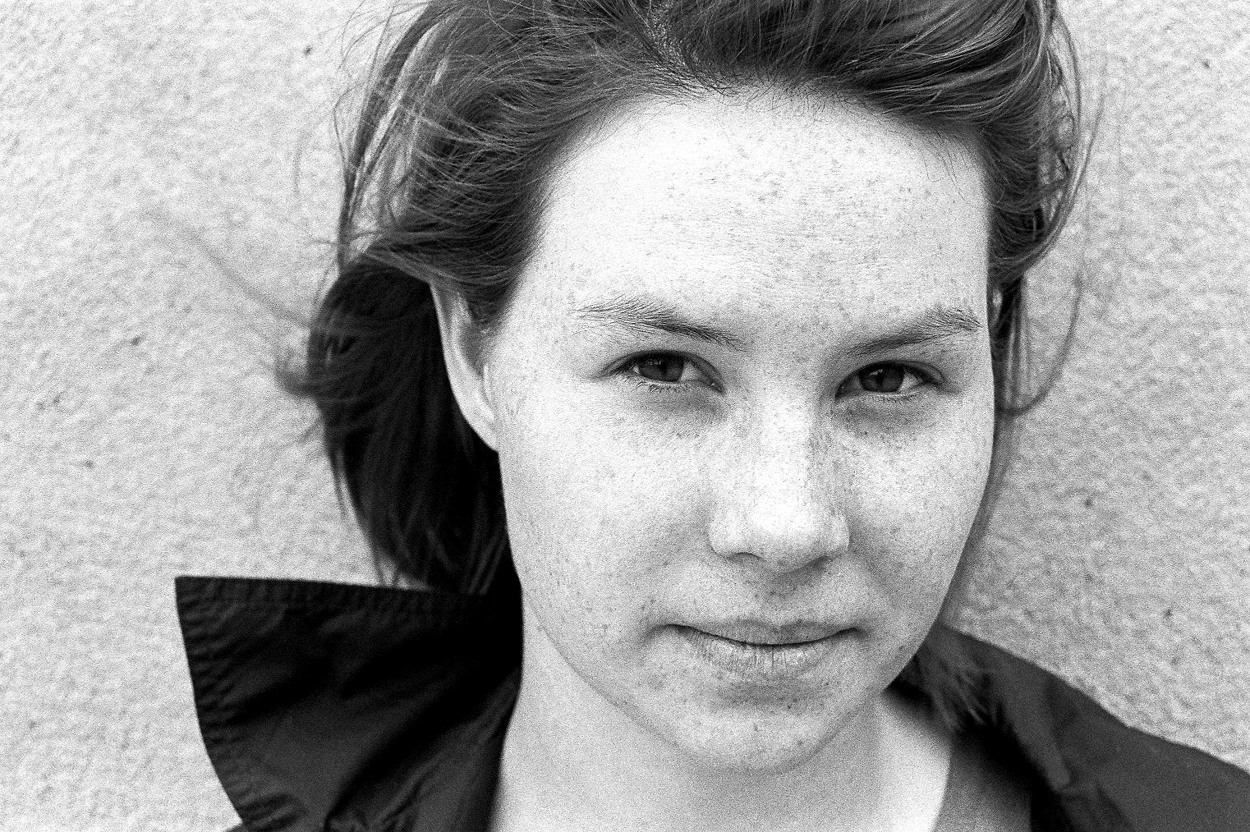 Close-up of a thoughtful young woman standing against a wall with her head turned to the side, in black and white.