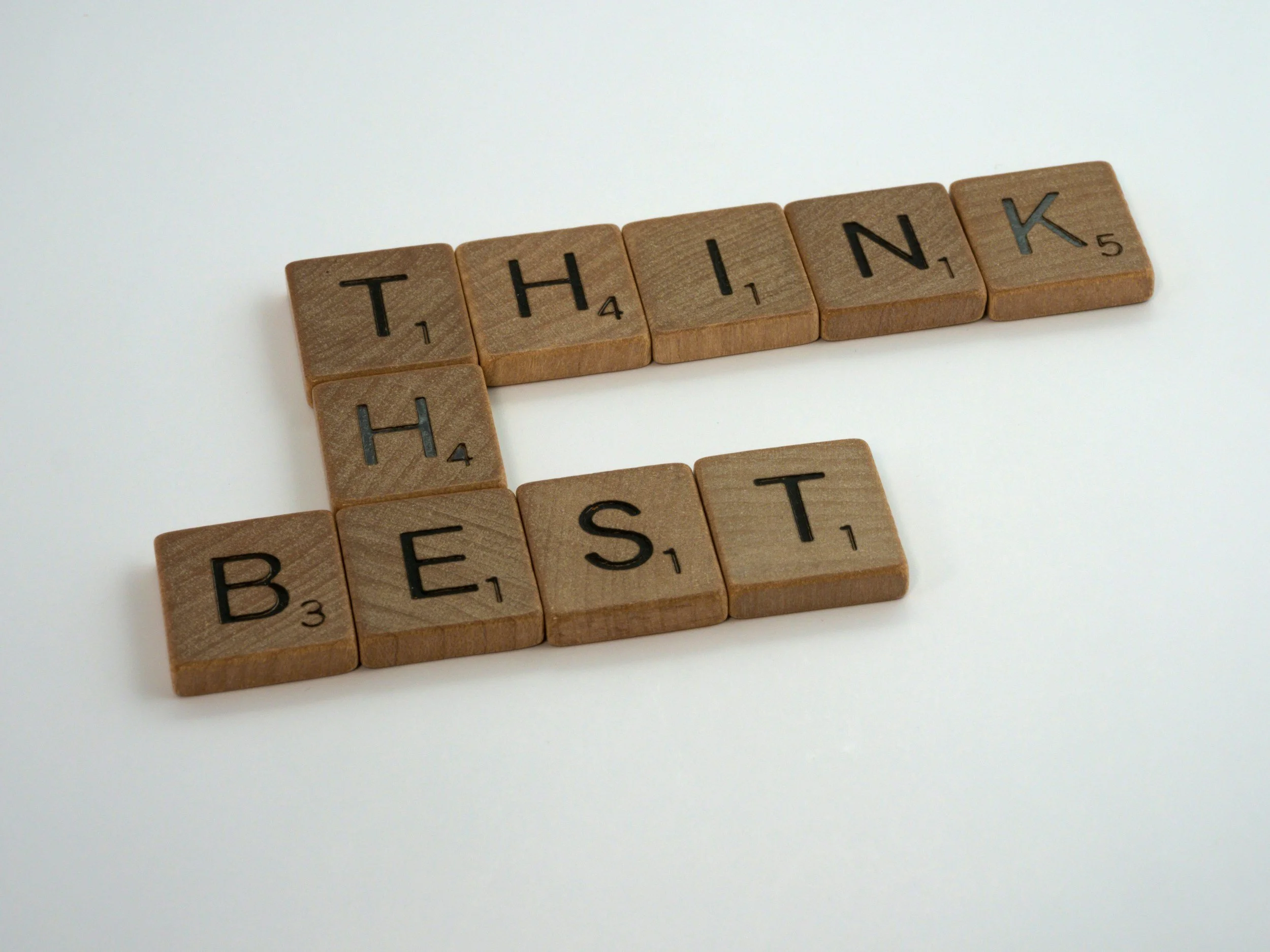 Wooden Scrabble tiles spelling 'THANKS' and 'BEST' on a white surface.