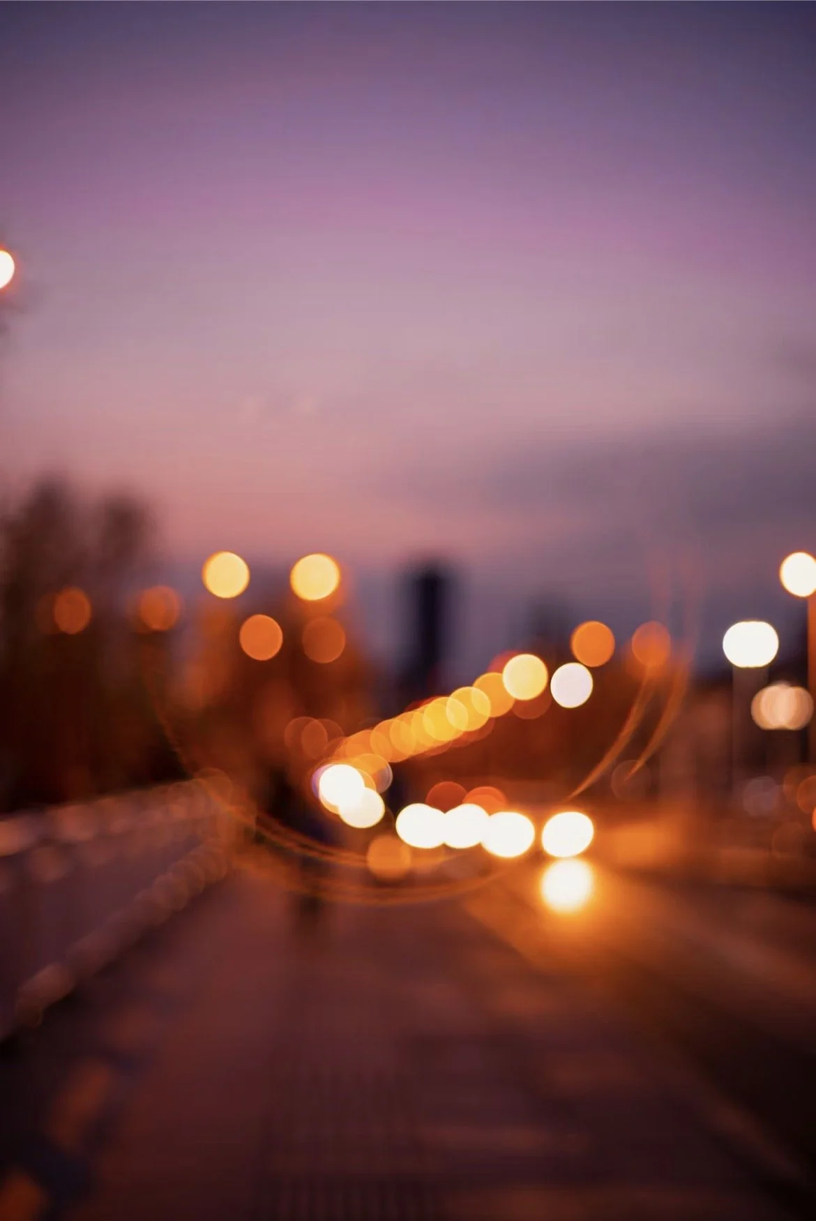 Blurred city street scene at dusk with streetlights and a purple sky.