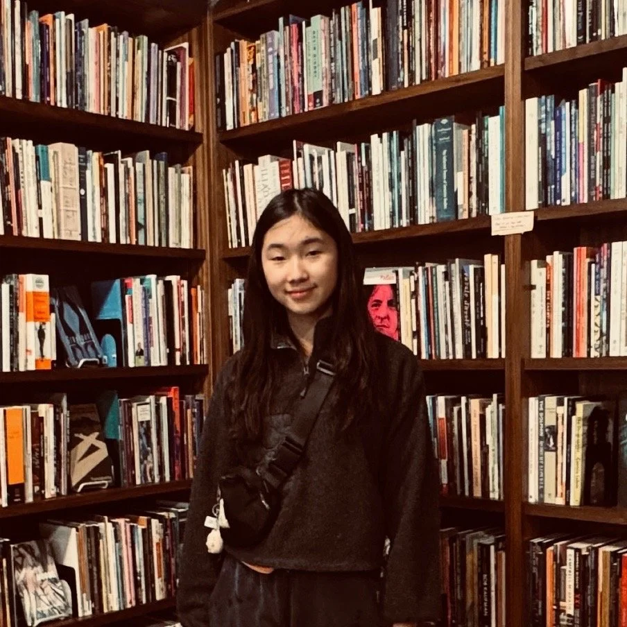 A young woman standing in front of wooden bookshelves filled with books in a bookstore or library.