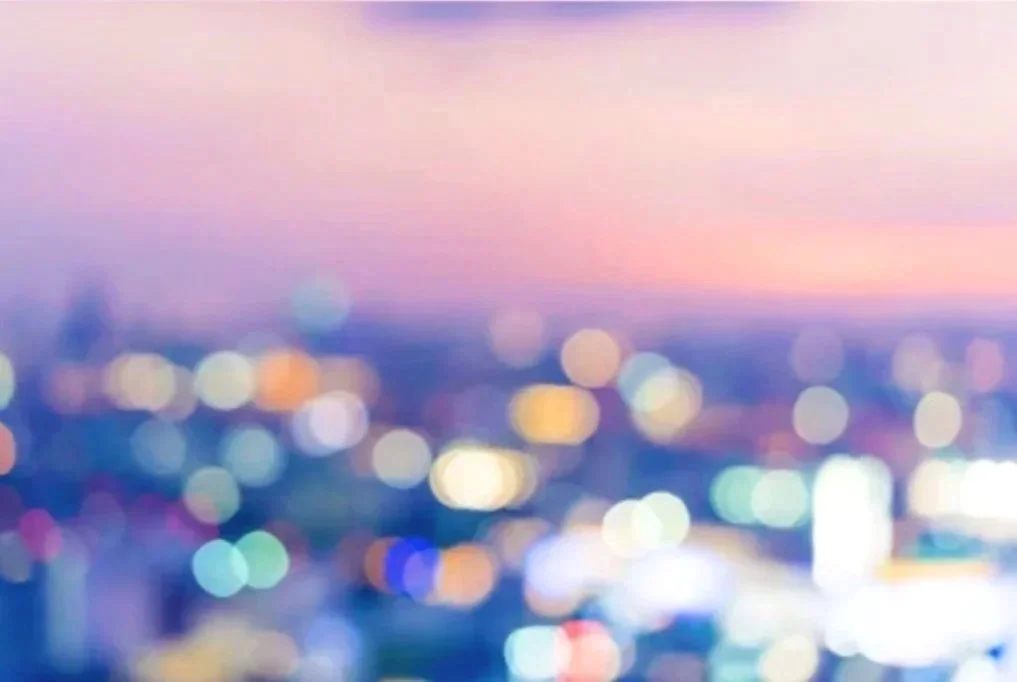Blurred cityscape at dusk with pastel sky and colorful bokeh lights.