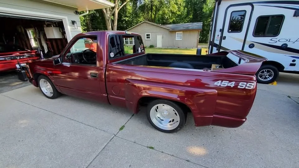 A red pickup truck with a lowered stance parked on a driveway. The truck has custom wheels and a '454 SS' decal on the rear side.
