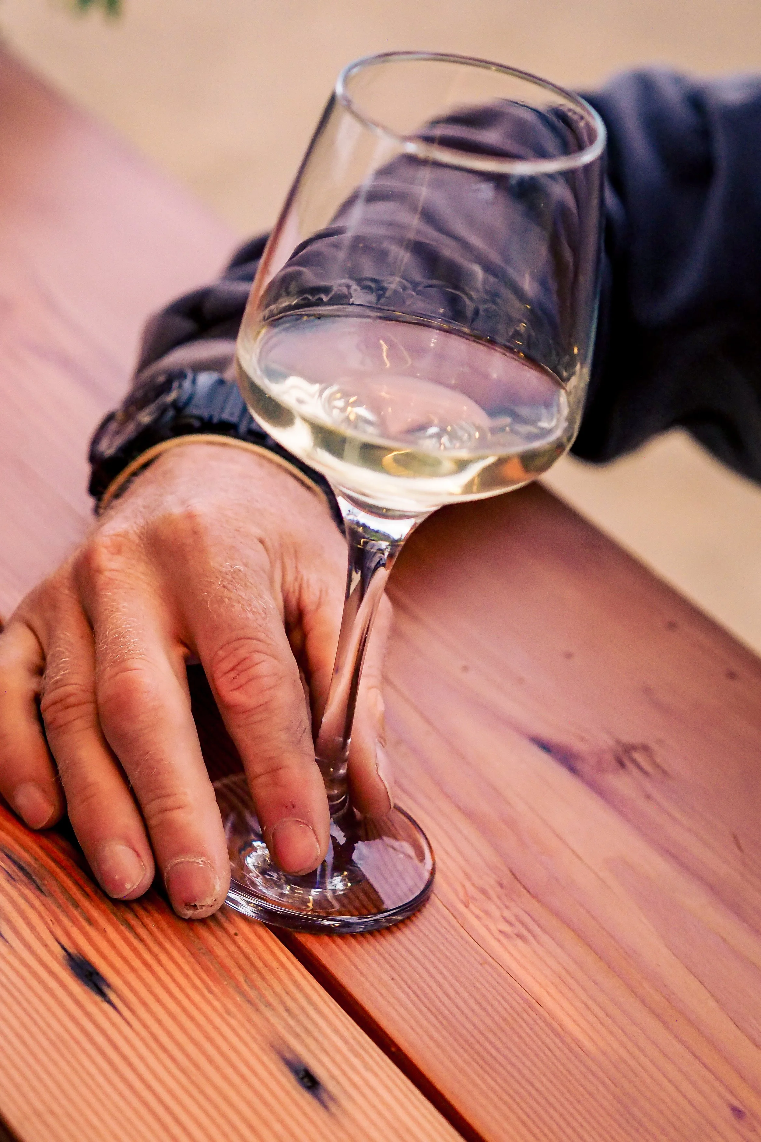 Person holding a glass of white wine over a wooden table.