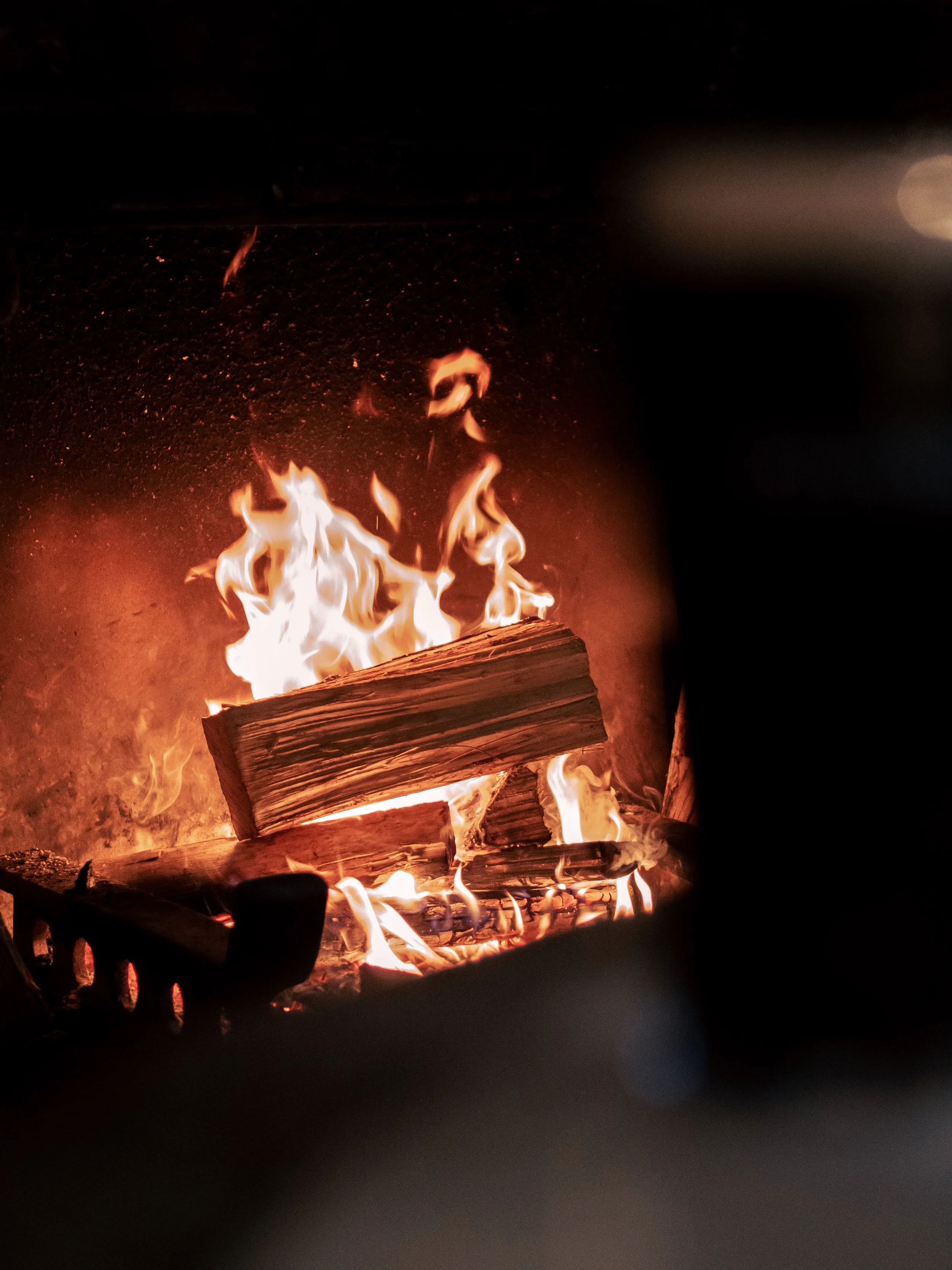 A close-up view of a wood fire with flames and burning logs in a dark setting.