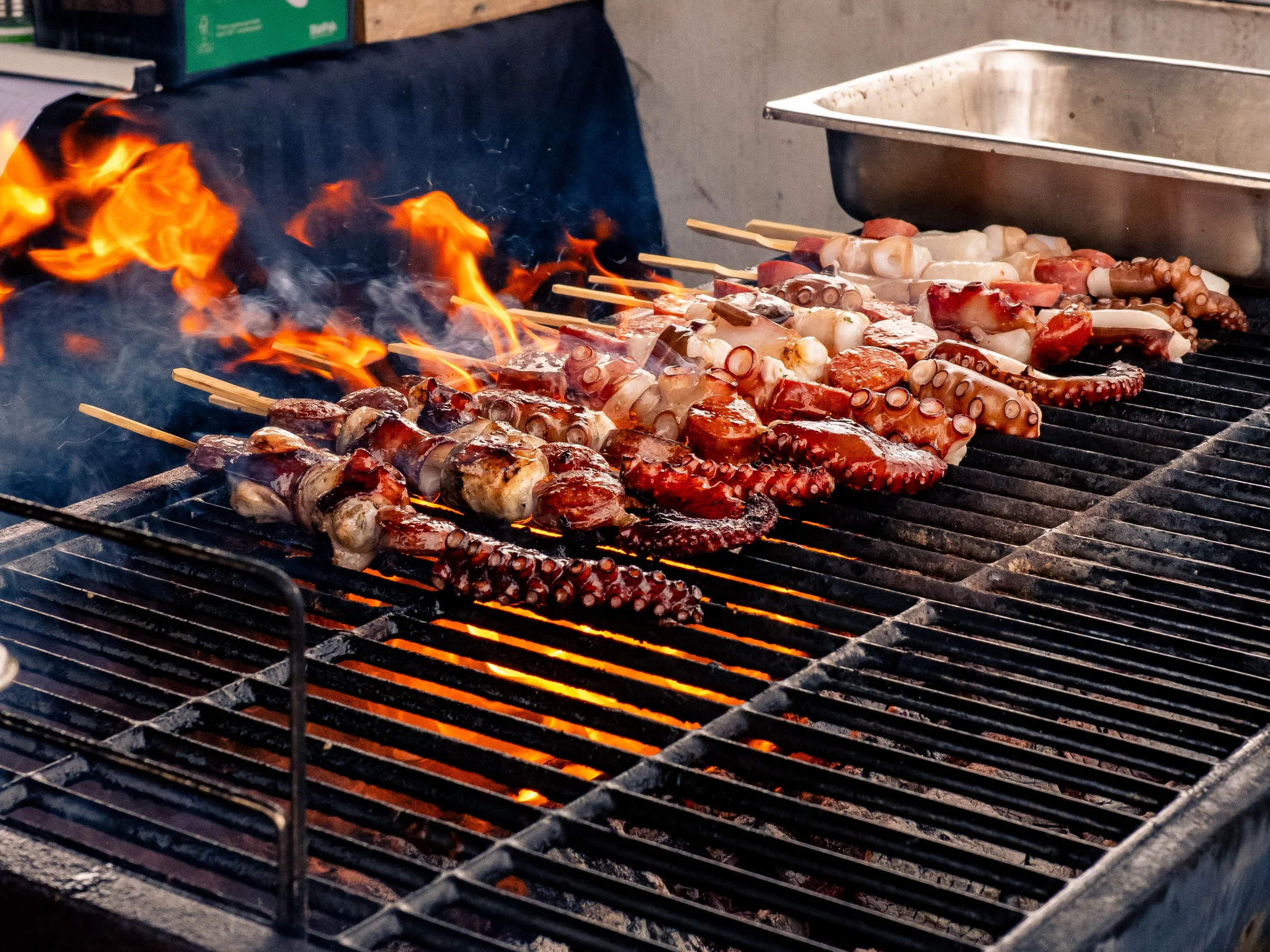 Skewered octopus and other seafood grilling over open flames on a barbecue grill.
