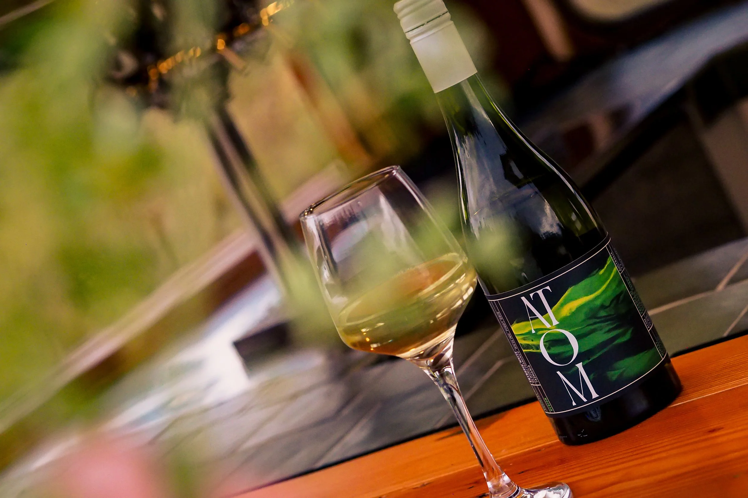 A wine bottle with a vibrant label, a glass of white wine, and a blurred background with green and brown tones.