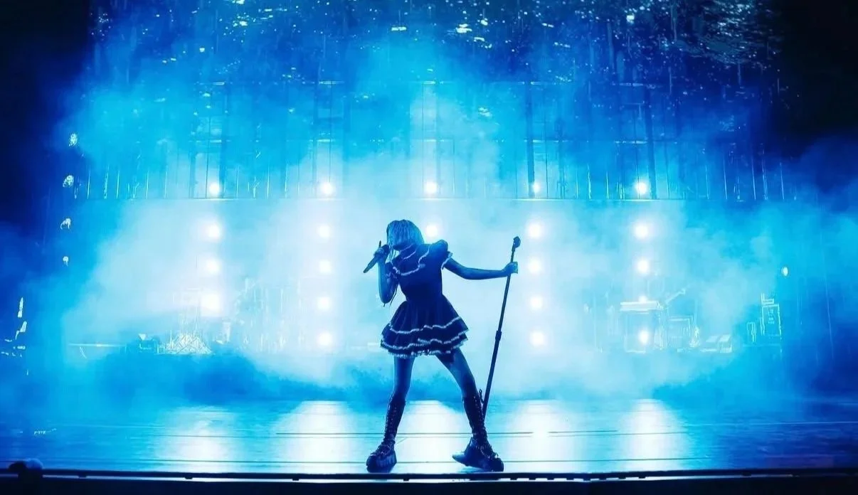 Halsey on stage with a microphone in one hand and a staff in the other, surrounded by blue lights and fog, creating a dramatic atmosphere.