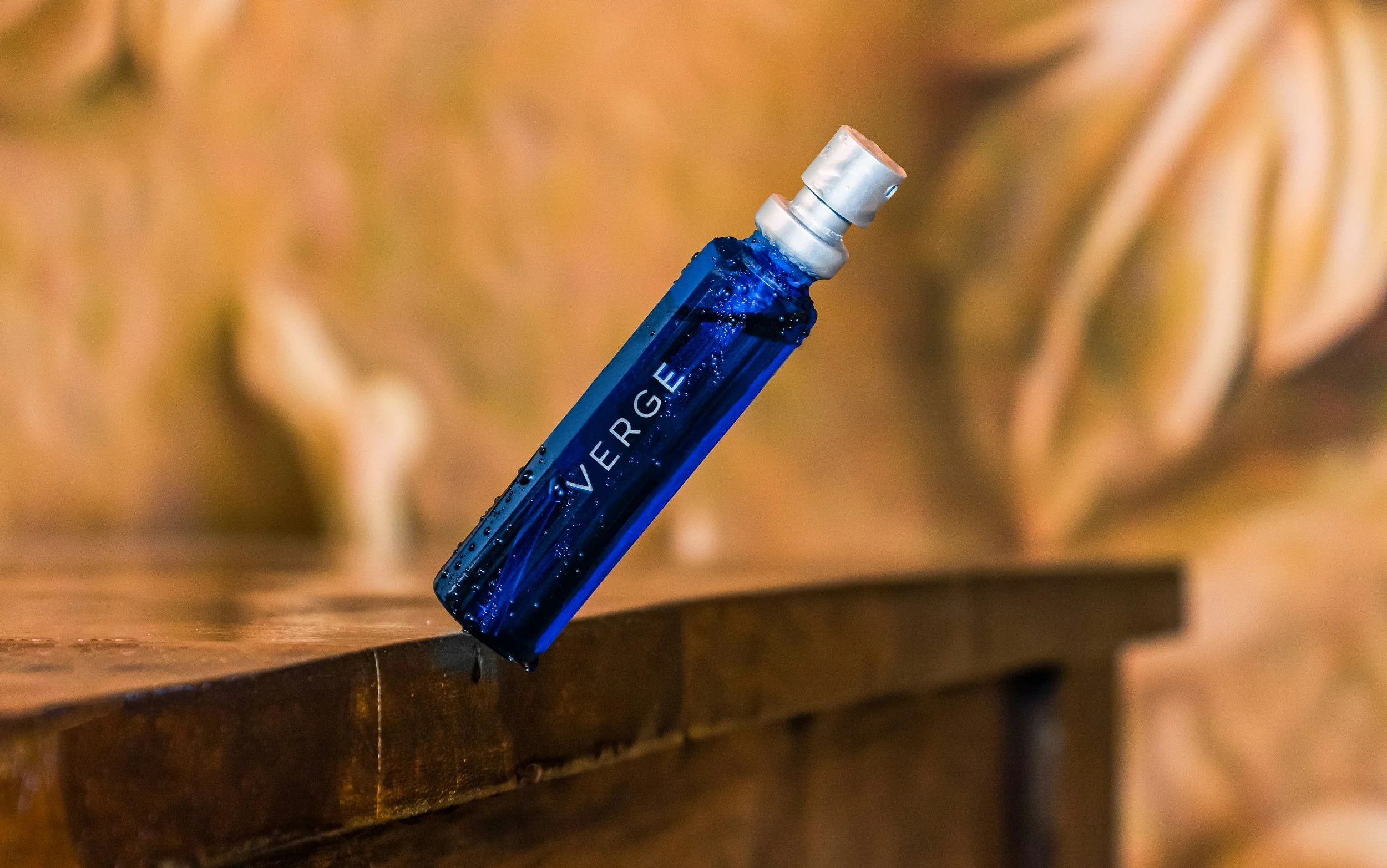A blue perfume spray bottle with the label 'VERGE' on a wooden surface.