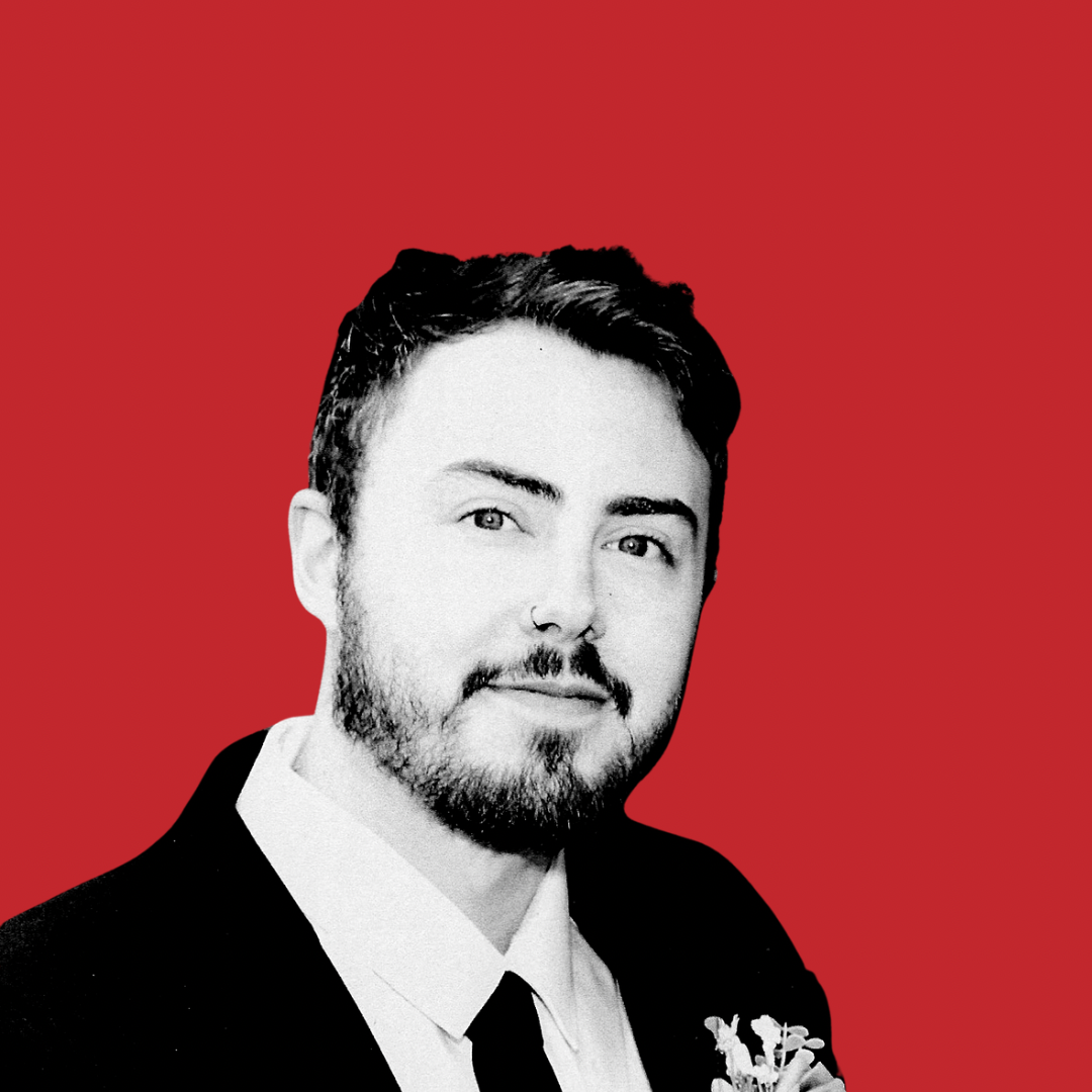 Black and white portrait of a young man with a beard and mustache, wearing a suit with a white shirt and black tie, against a red background.