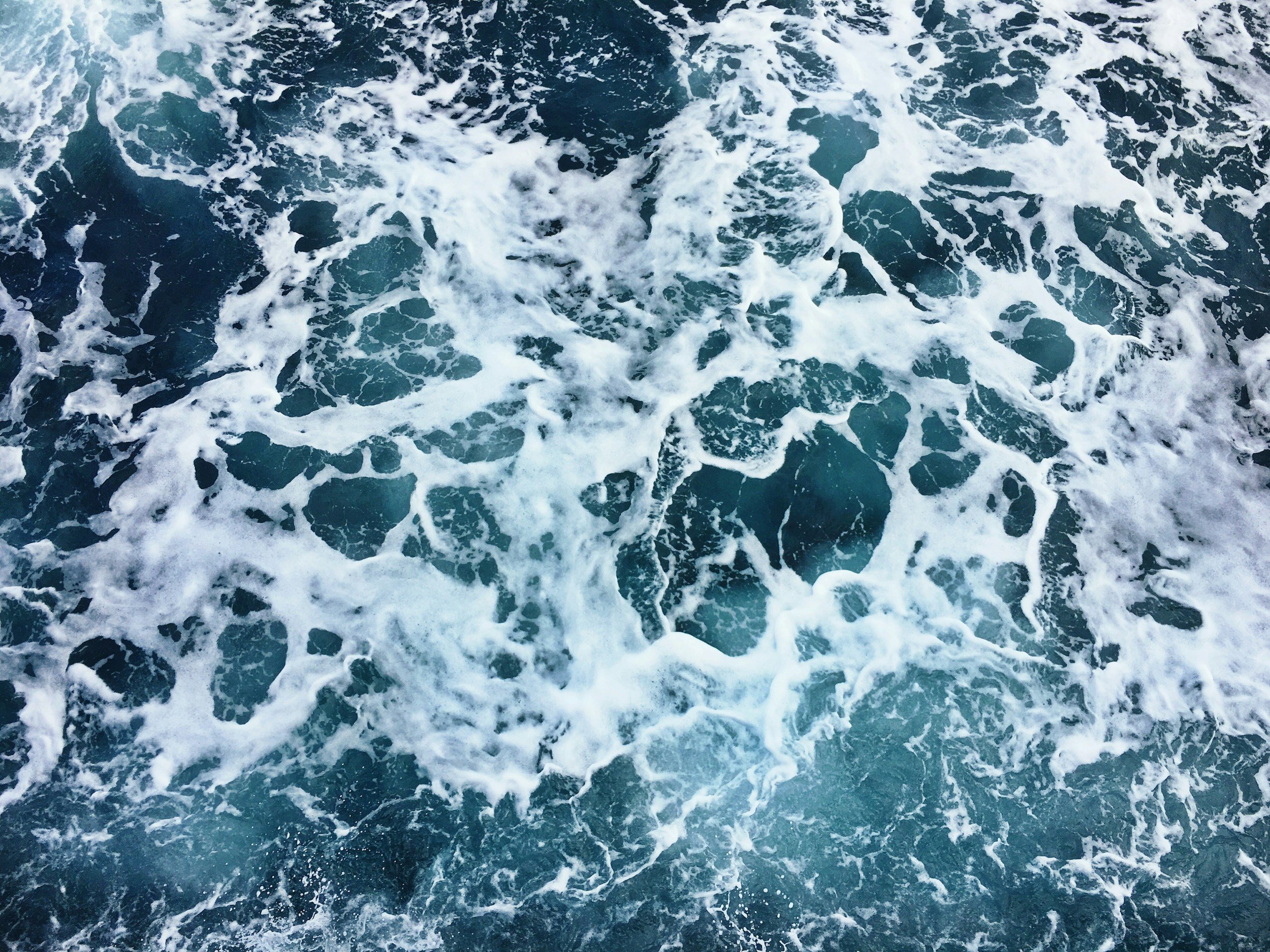 Churning ocean water with white foam, seen from above.