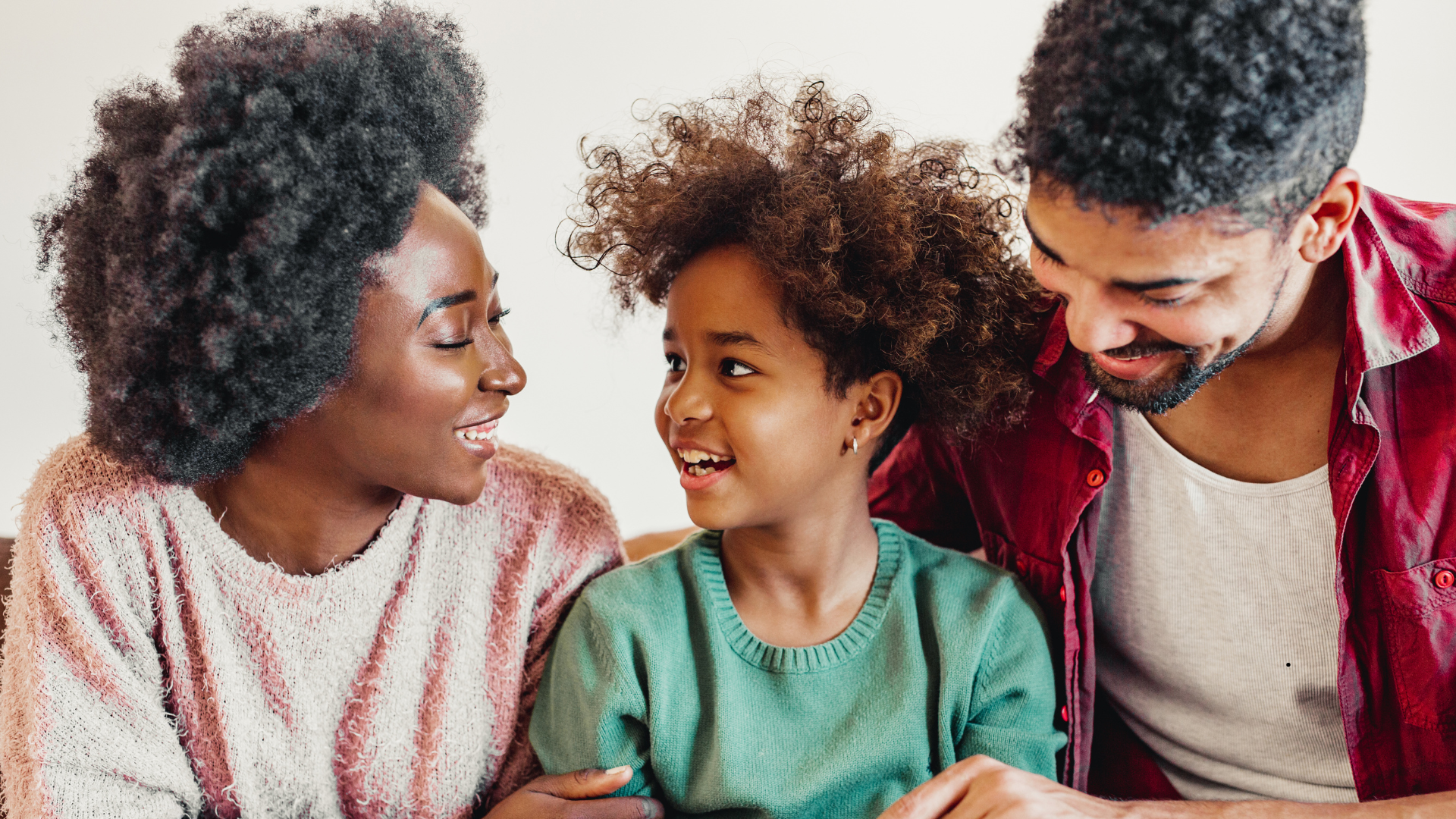A family of three, including a woman, a man, and a young girl, sharing a happy moment together, smiling and talking closely.