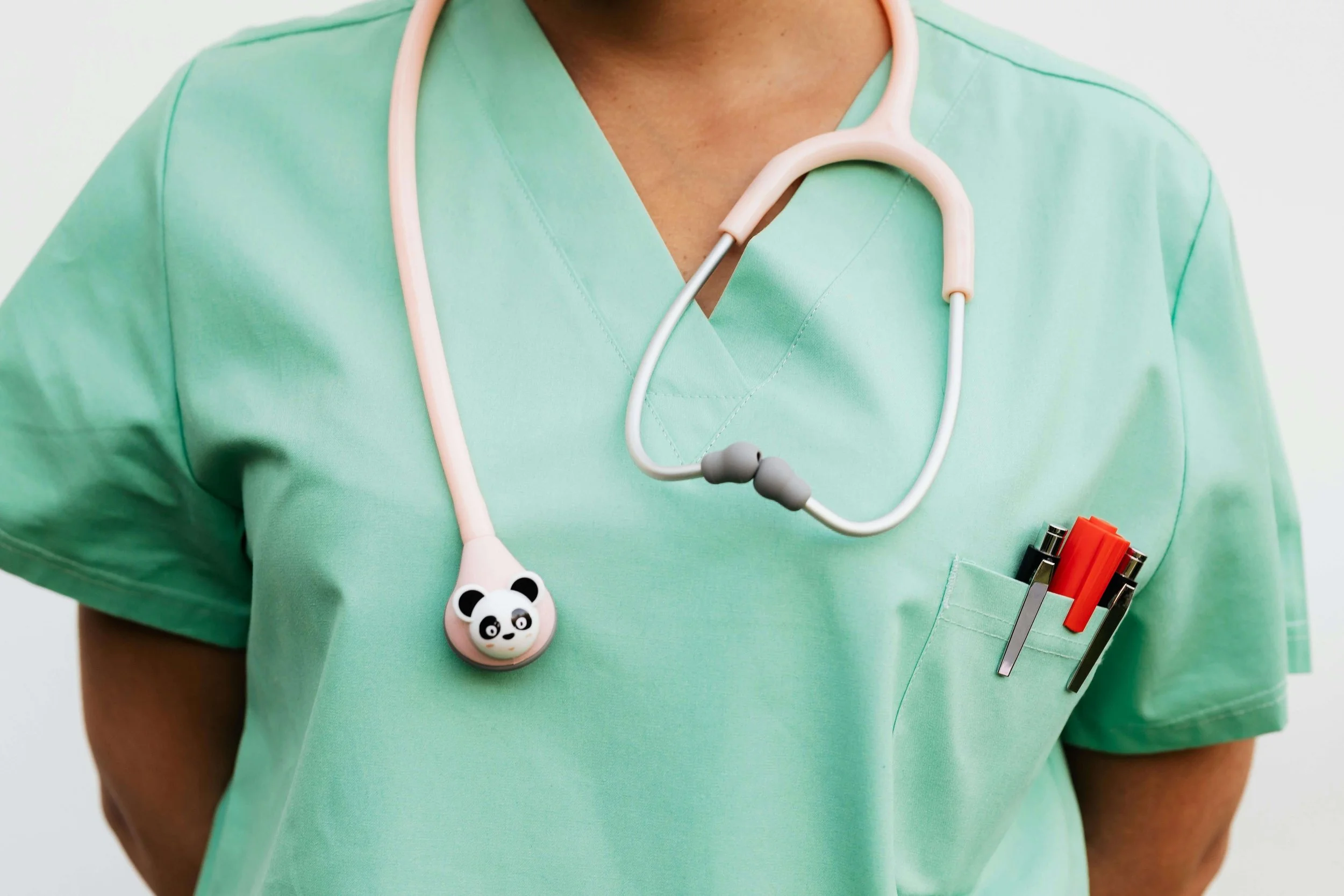 Medical professional wearing green scrubs with a stethoscope and pens in the pocket, close-up of the upper body.