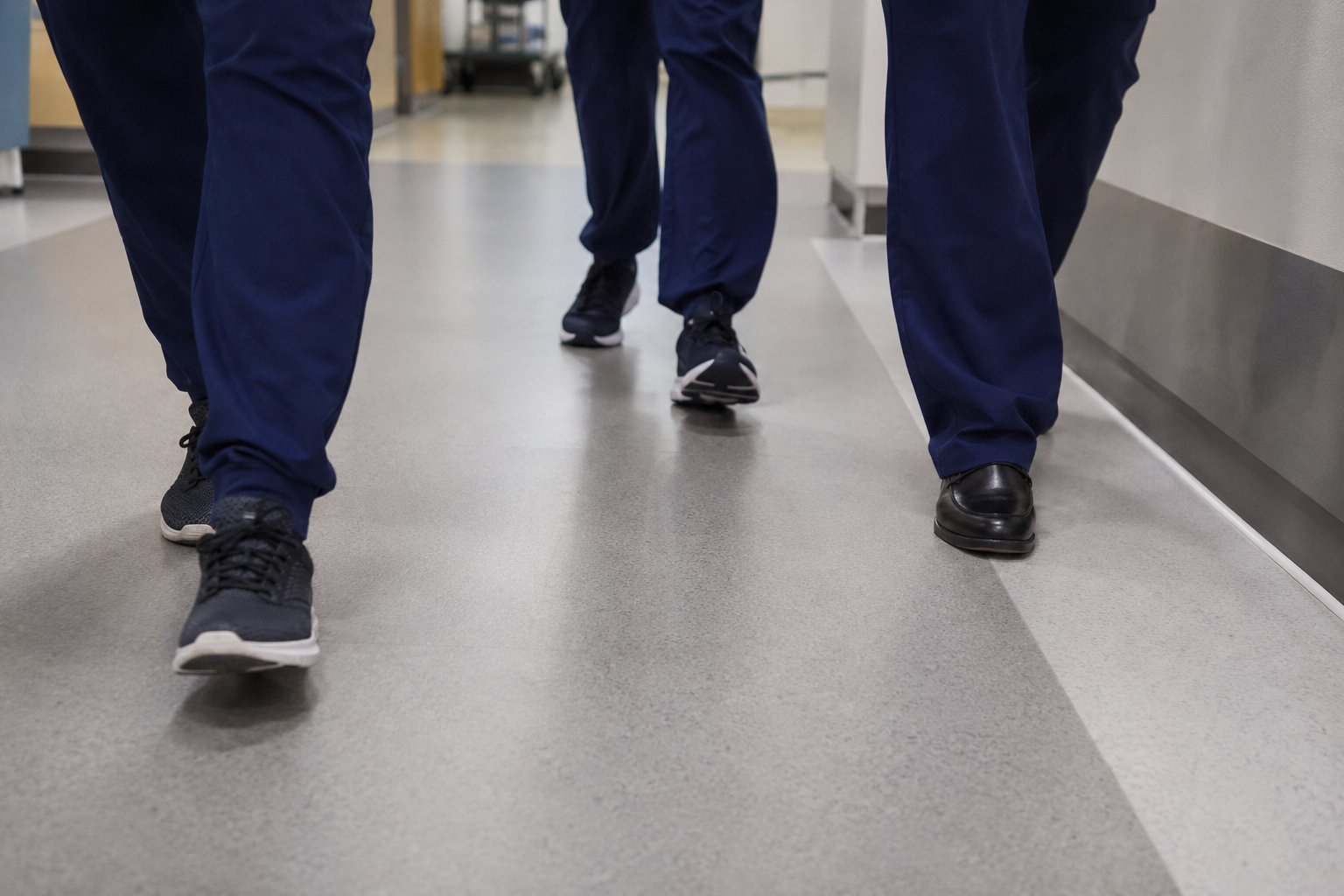 People walking in a hallway, wearing dark blue uniforms and athletic shoes.
