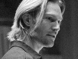 Black and white photo of a young man with shoulder-length hair, looking to the side.