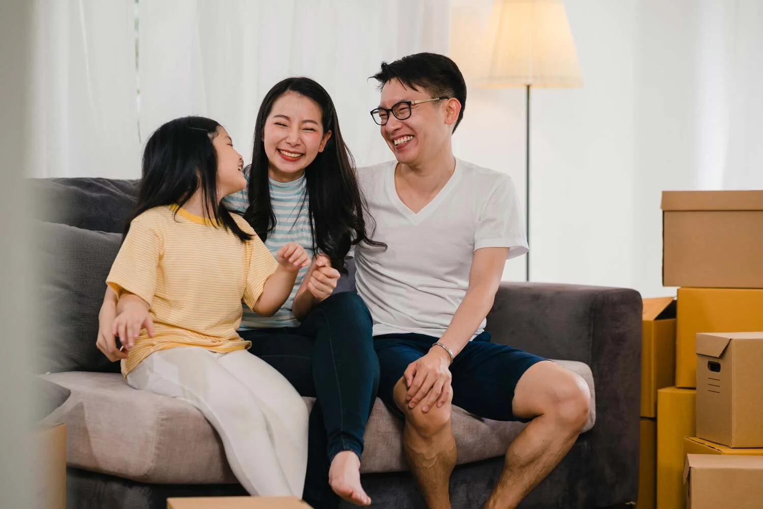 happy-asian-young-family-homeowners-bought-new-house-japanese-mom-dad-daughter-embracing-looking-forward-future-new-home-after-moving-relocation-sitting-sofa-with-boxes-together-copy.jpg