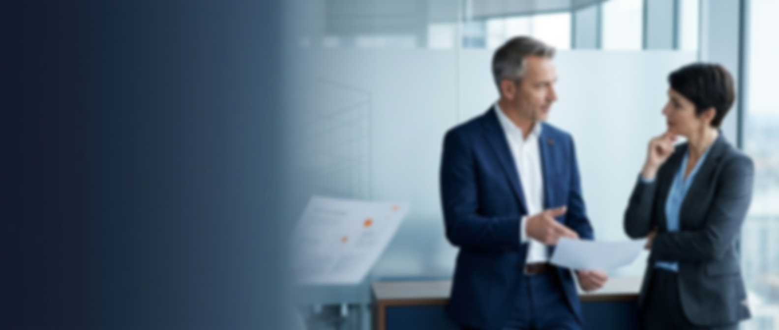Two professionals, a man and a woman, having a discussion in an office with large windows, holding papers.