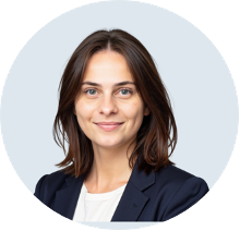 Portrait of a woman with shoulder-length brown hair, wearing a navy blazer and white top, smiling against a light background.