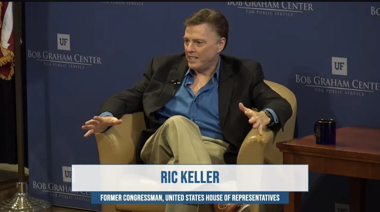 Ric Keller, a former Congressman from the U.S. House of Representatives, sitting in a beige armchair during an interview at the Bob Graham Center for Public Service. The background features a blue wall with the center's logo.
