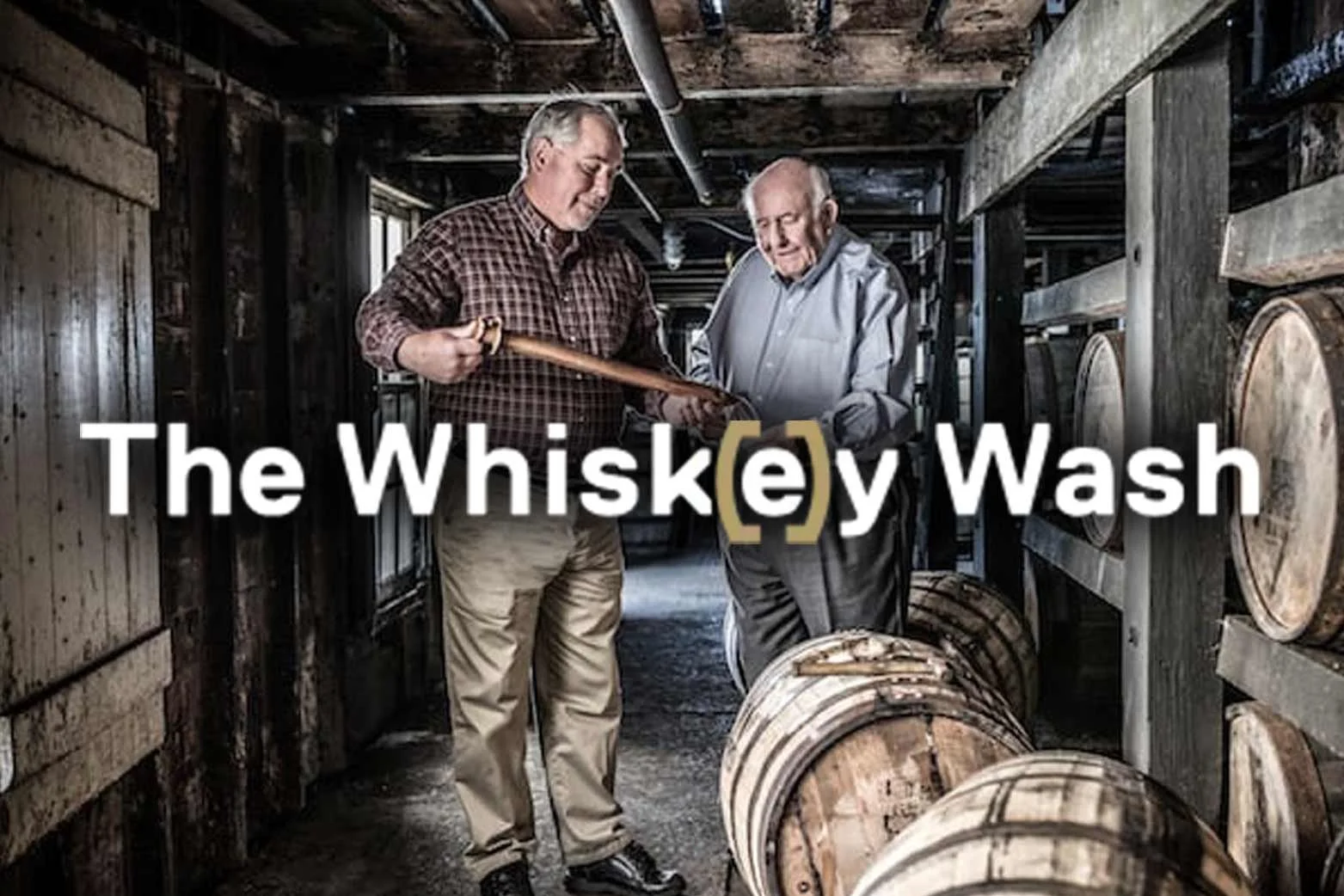 Two men in a whiskey aging cellar, surrounded by wooden barrels, discussing and inspecting a whiskey aging process.